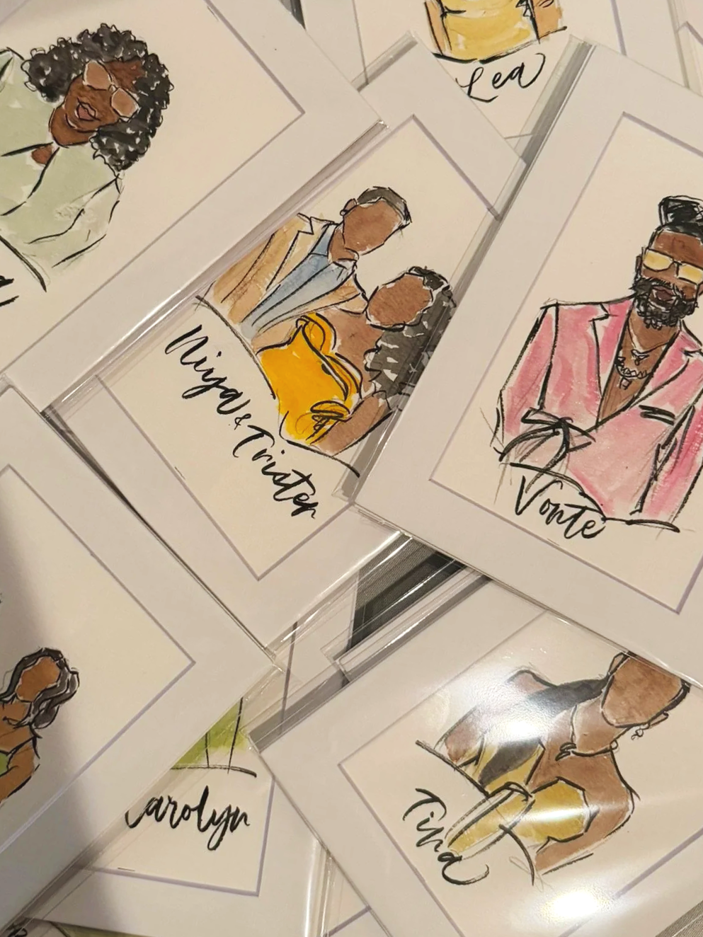 Watercolor portraits of women with names, displayed on a wooden table.