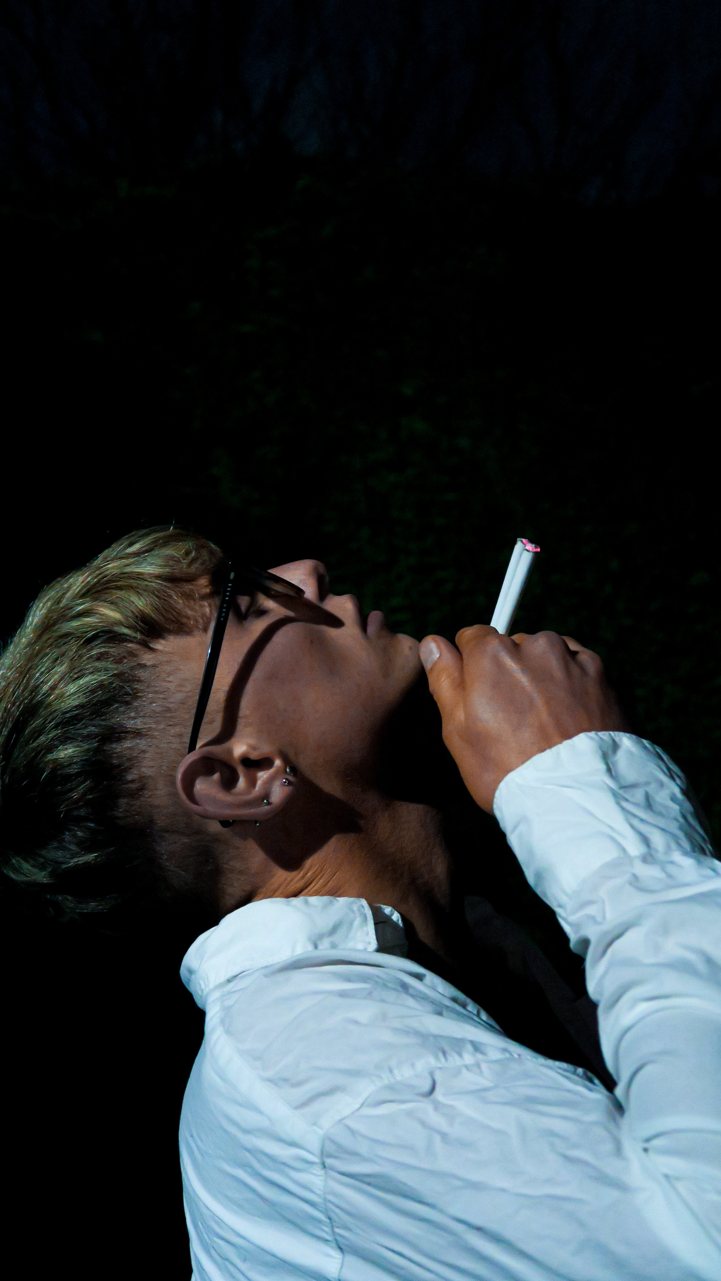 A person with glasses and earrings smoking a cigarette at night.