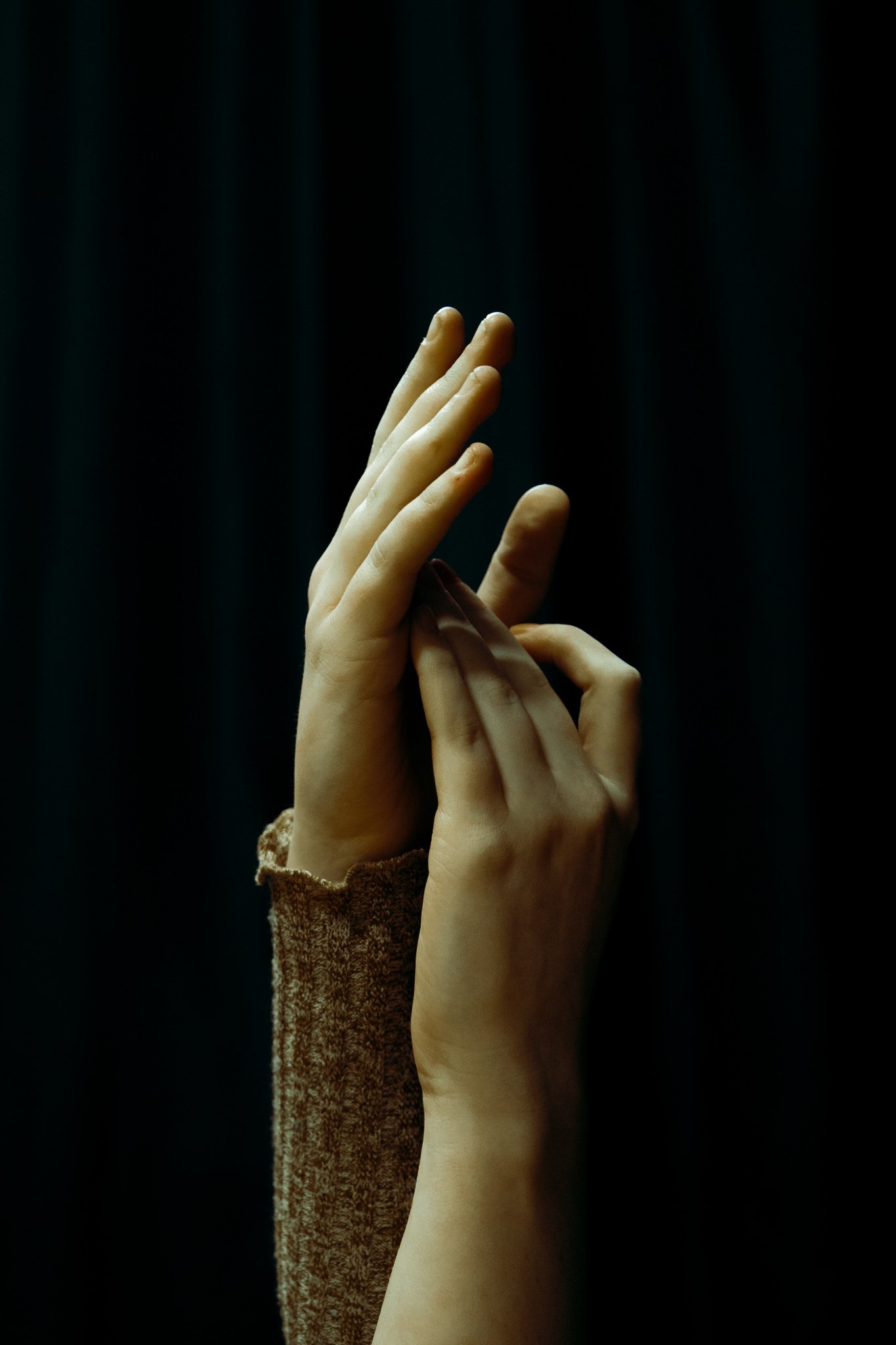 Two hands with fingers intertwined, one hand with a brown sleeve, against a dark background.