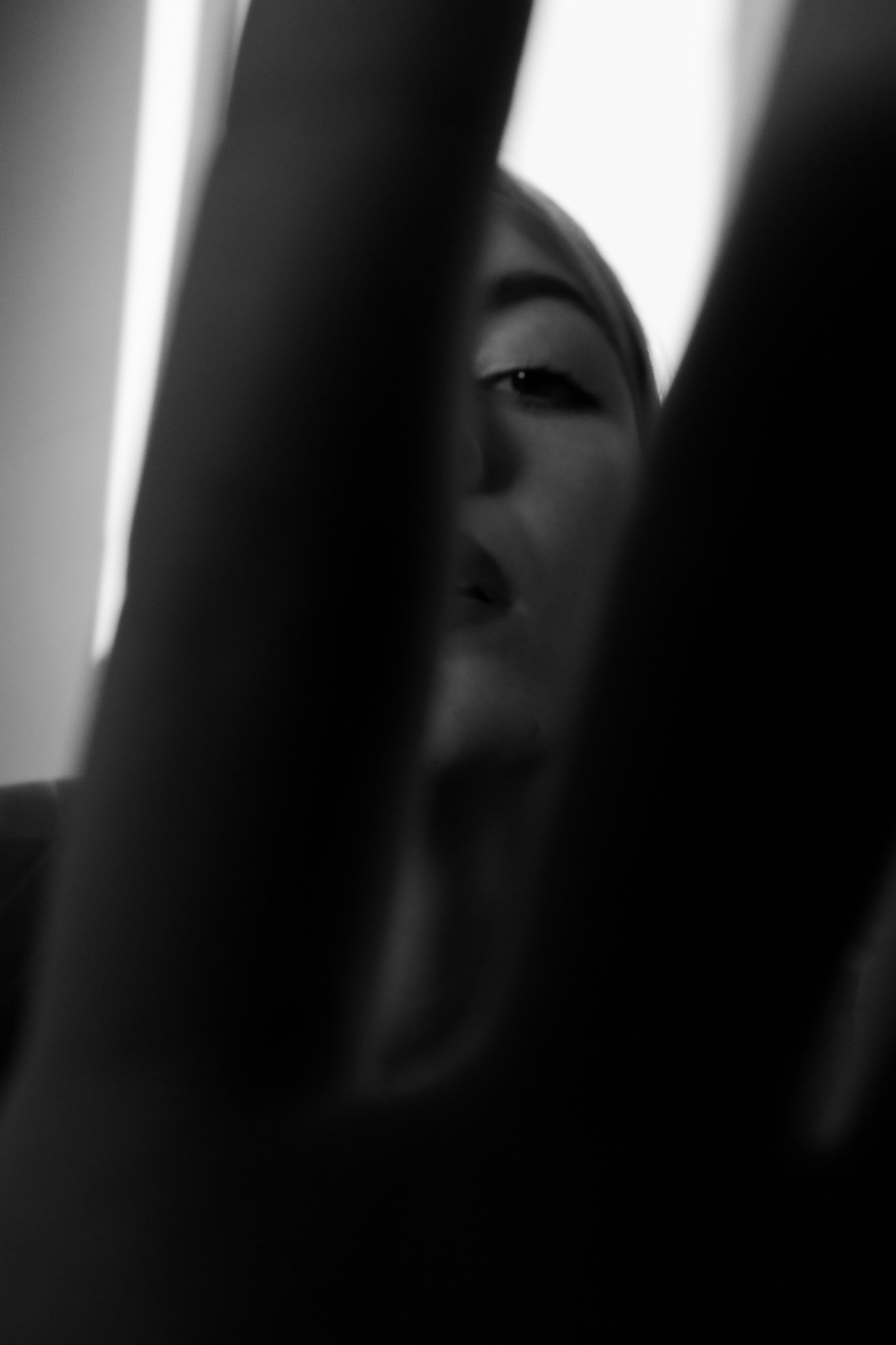 Close-up black and white photo of a woman's face partially obscured by dark vertical bars, with only one eye visible.