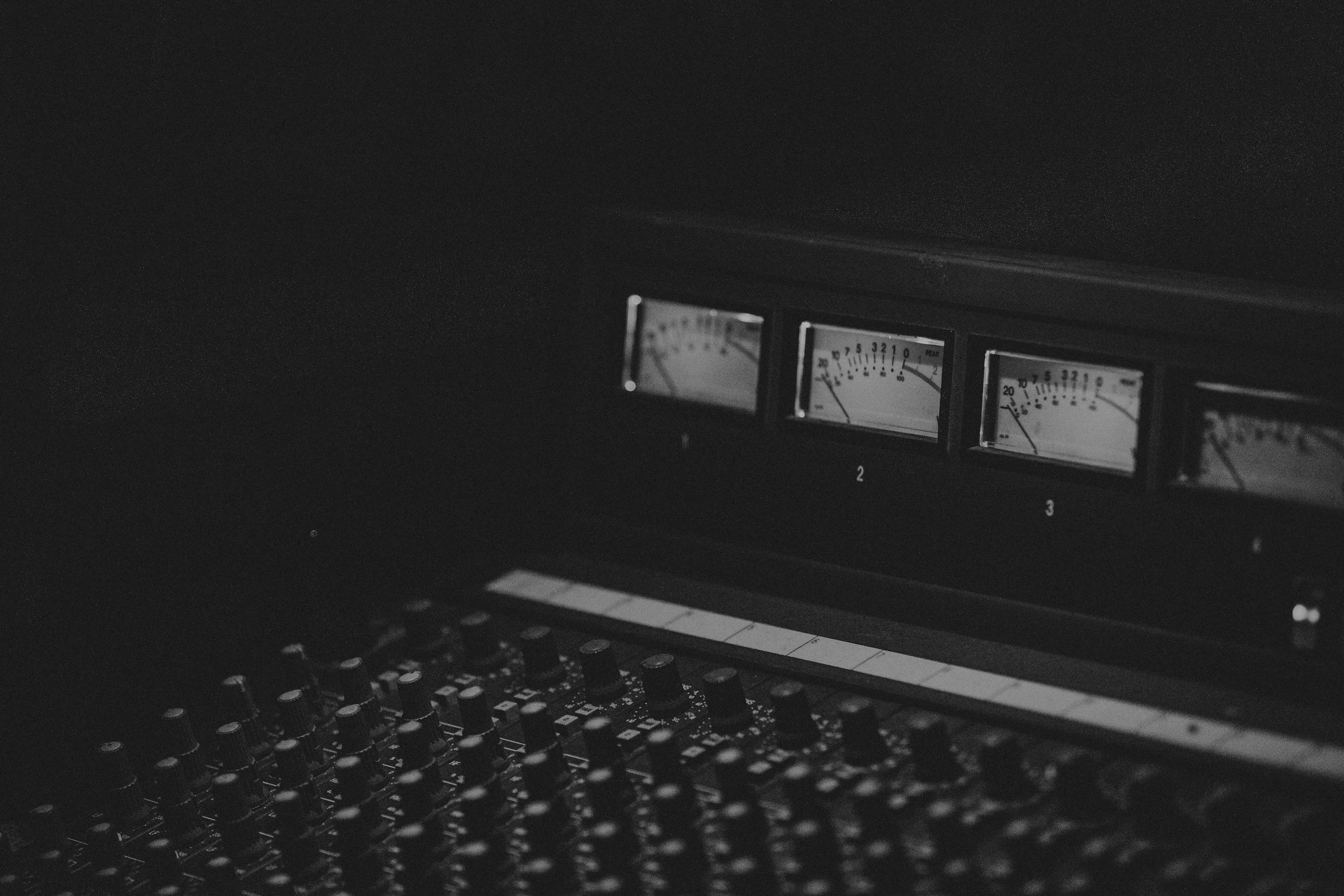 Black and white photo of an old audio mixing console with several meters showing levels and a keyboard below.