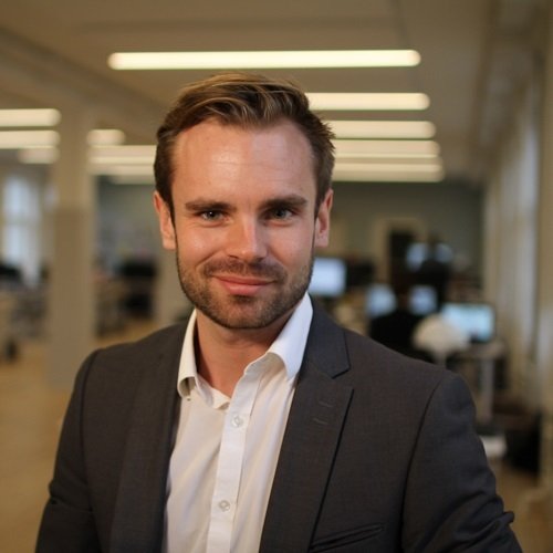 Lars Corvinius Olesen, Press Officer and Digital Coordinator at Dyrenes Alliance. In the picture, Lars is in a grey blazer, and white shirt with an office environment in the background. He is ready to help the animals.