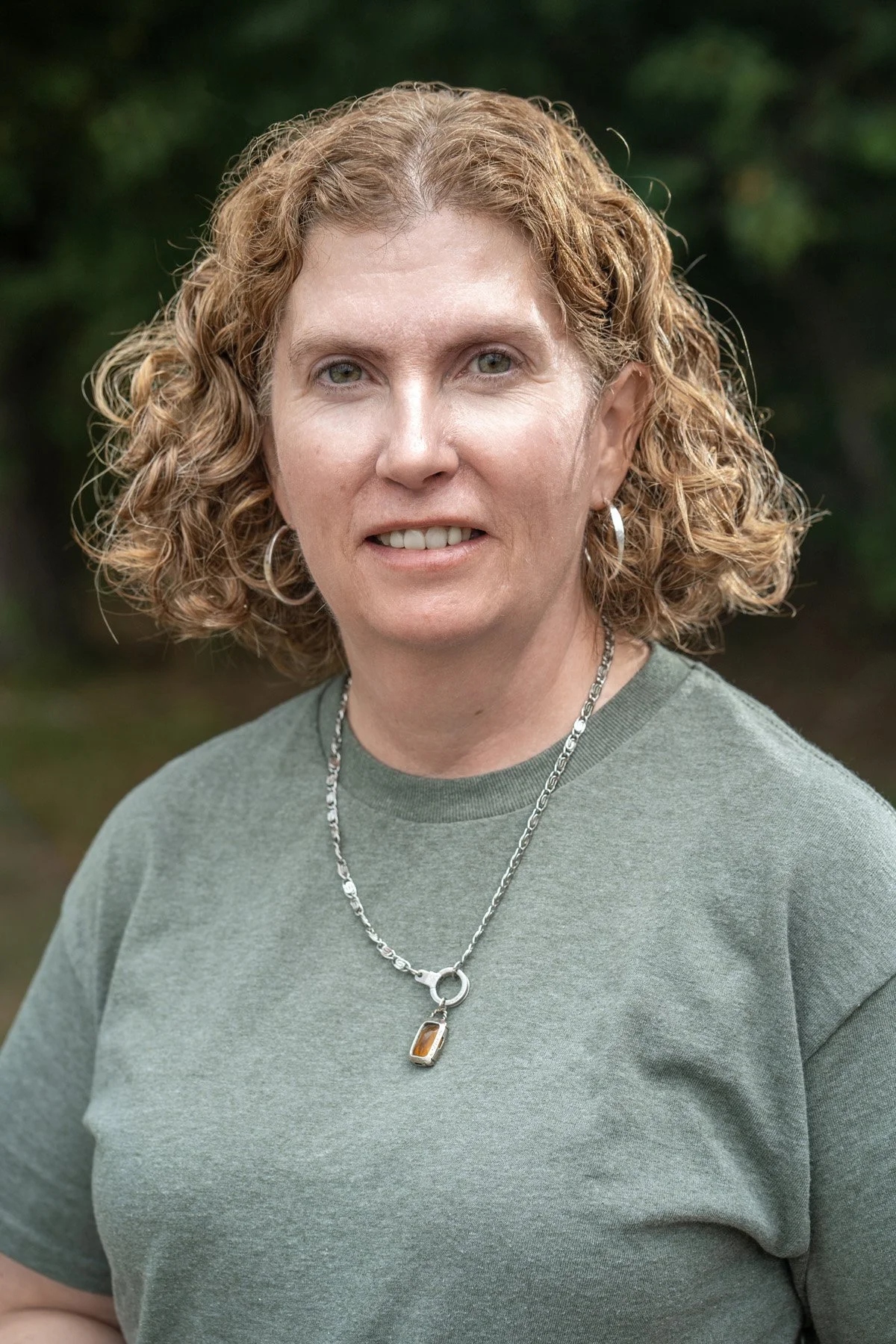 A man with dark curly hair, glasses, and a beard, looking to his left in a room with a plant and a photo on the wall in the background.