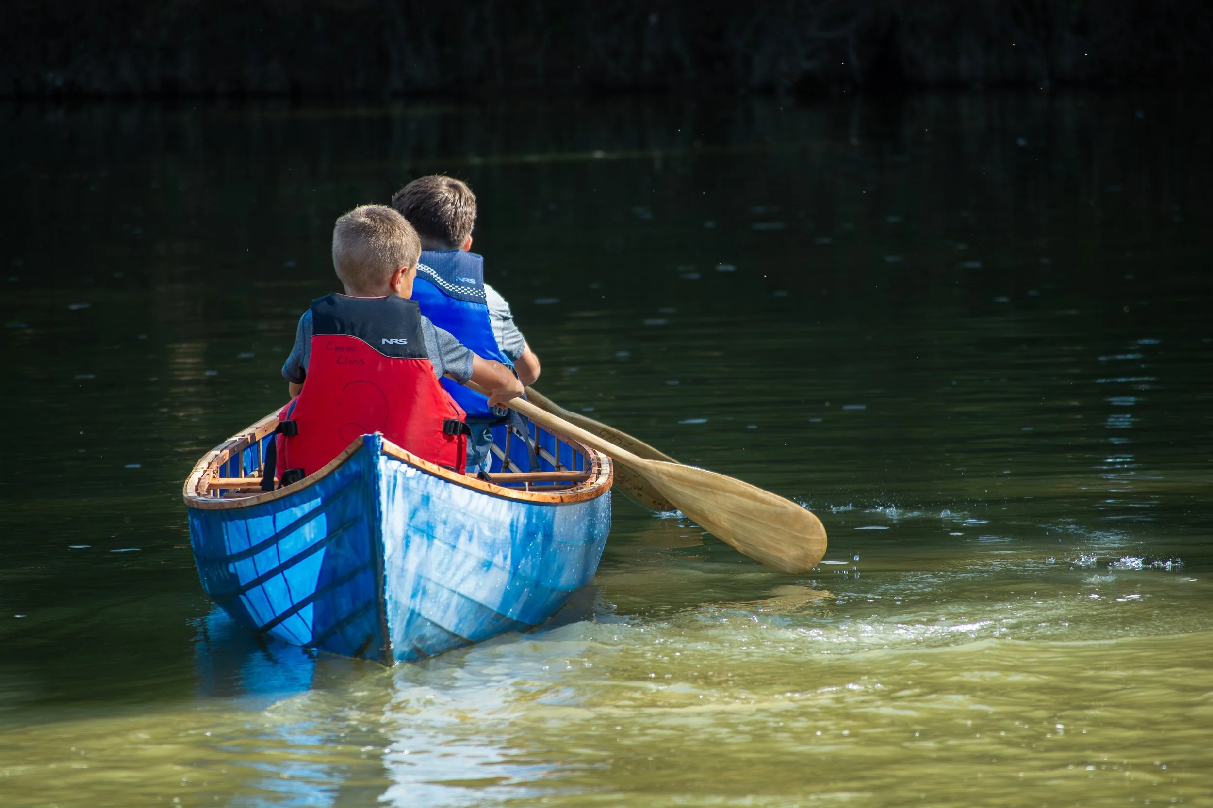 Two children in a canoe paddling on calm water during daytime