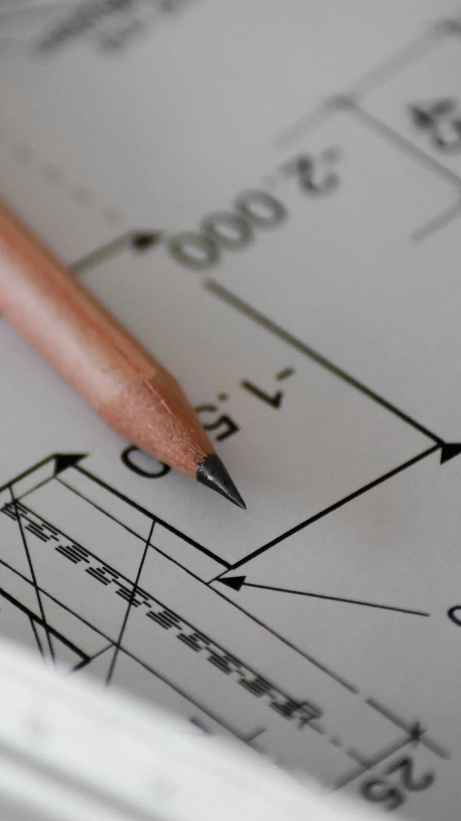 Close-up of a pencil on technical drawing paper with arrows and measurements.