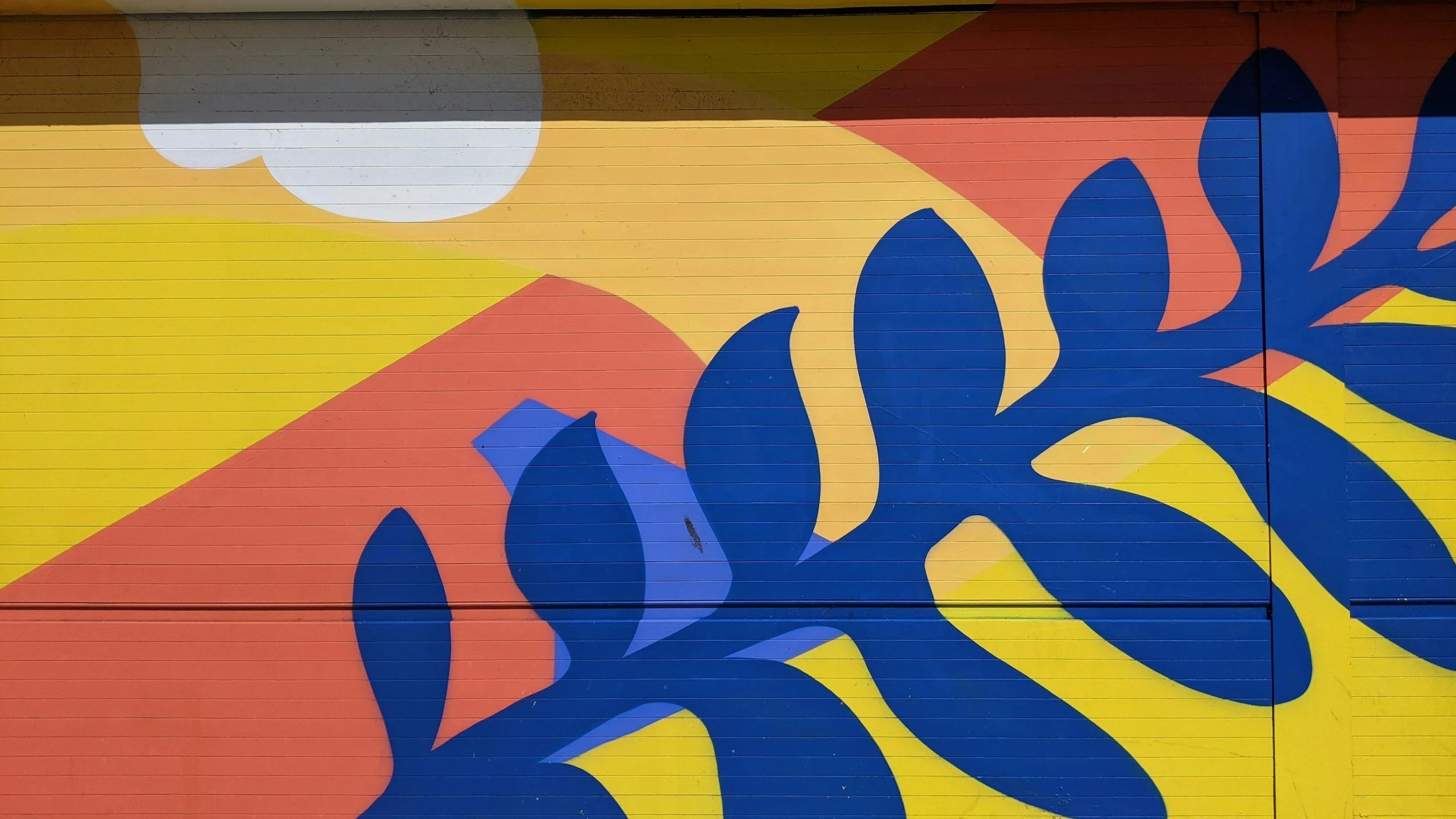 Colorful abstract mural with blue leaf shapes and a sun-like design on a wall.