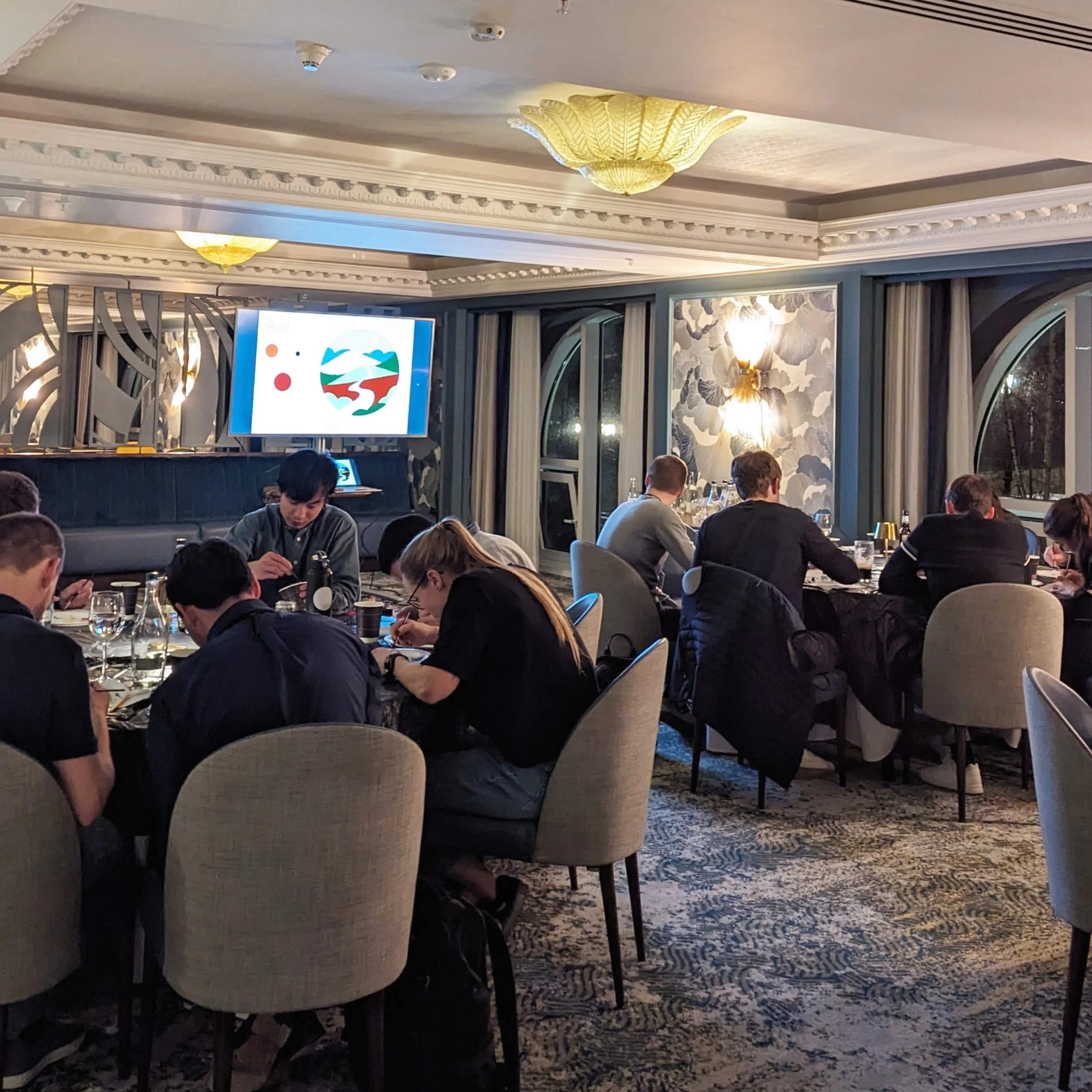 People sitting in a restaurant or conference room dining and looking at a presentation screen.