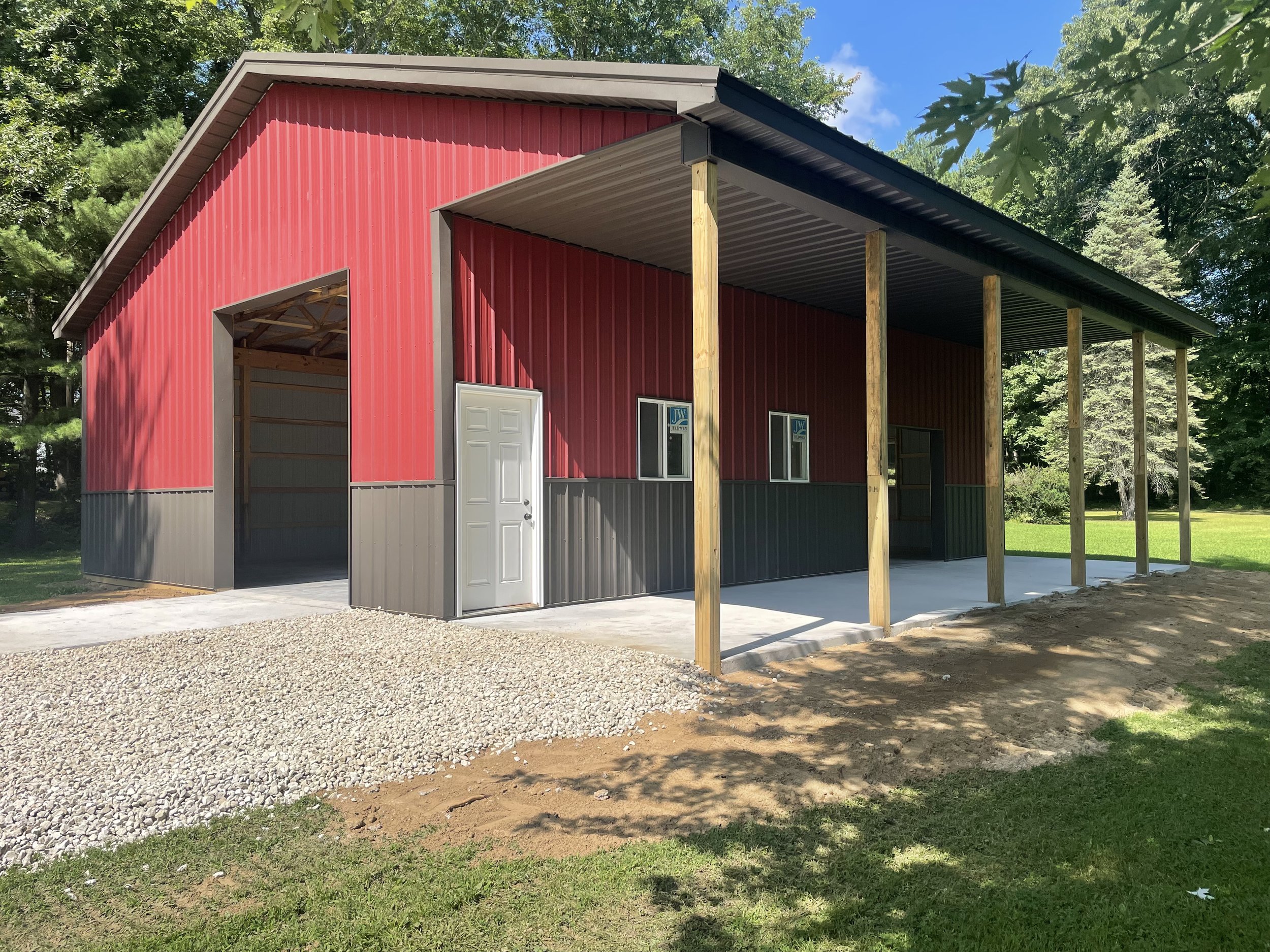 A red pole barn with concrete foundation, windows, and a white door.