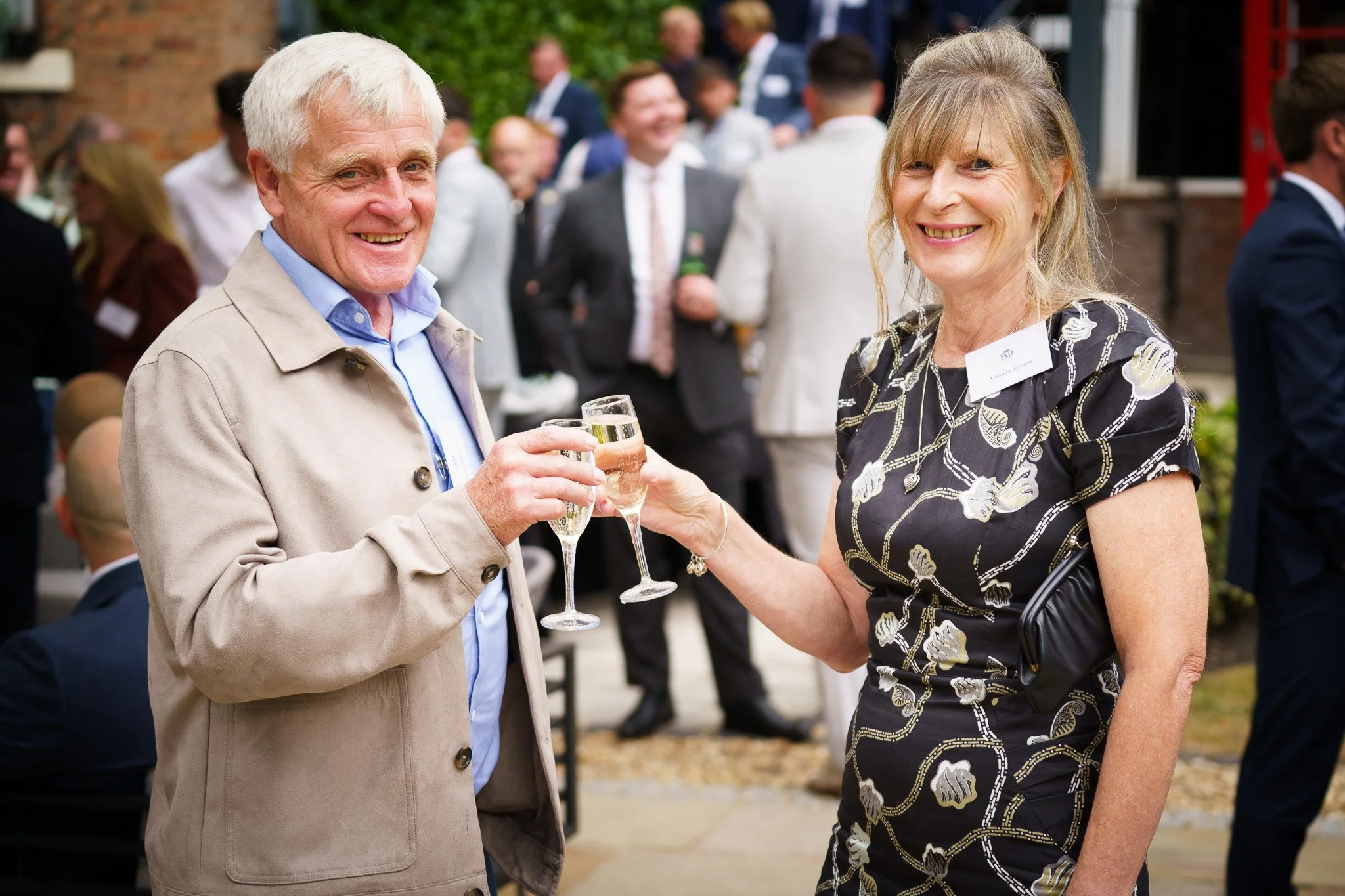 Portrait of a man and a woman holding wine glasses and smiling at an outdoor social event in Chester, Cheshire