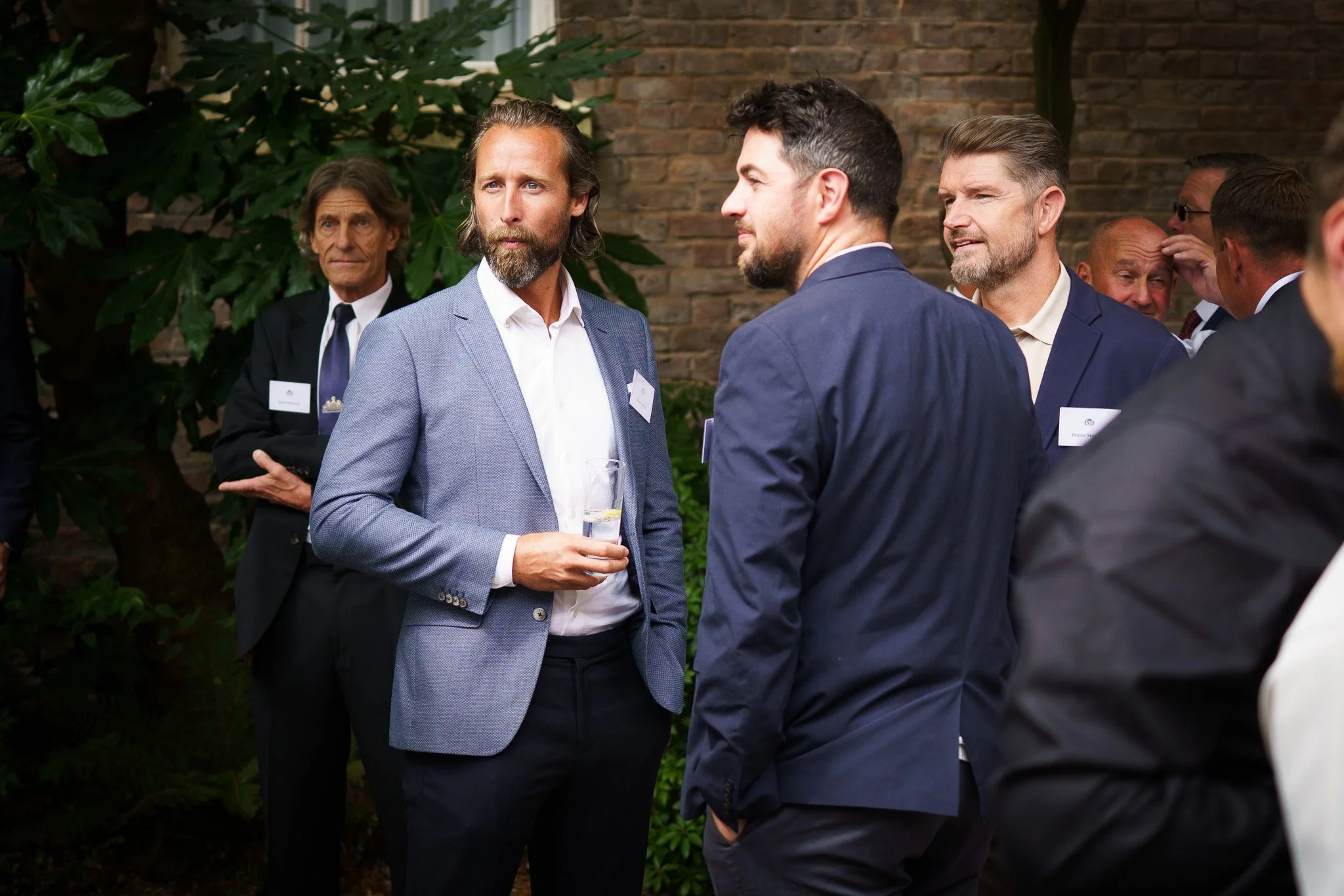 A group of six men in business suits engaged in conversation at an outdoor social event in Chester, Cheshire