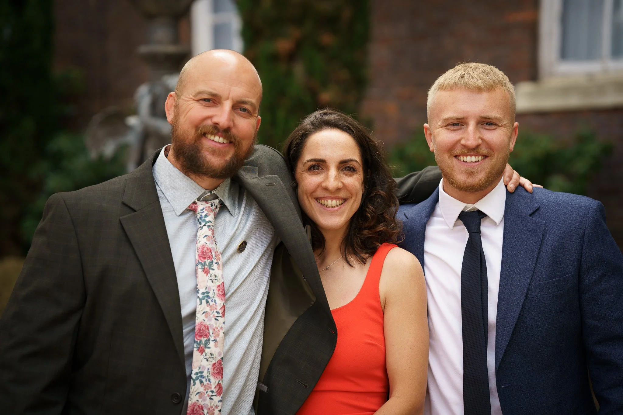 Candid portrait of Three people smiling, dressed in formal attire, at an outdoor social event in Chester, Cheshire