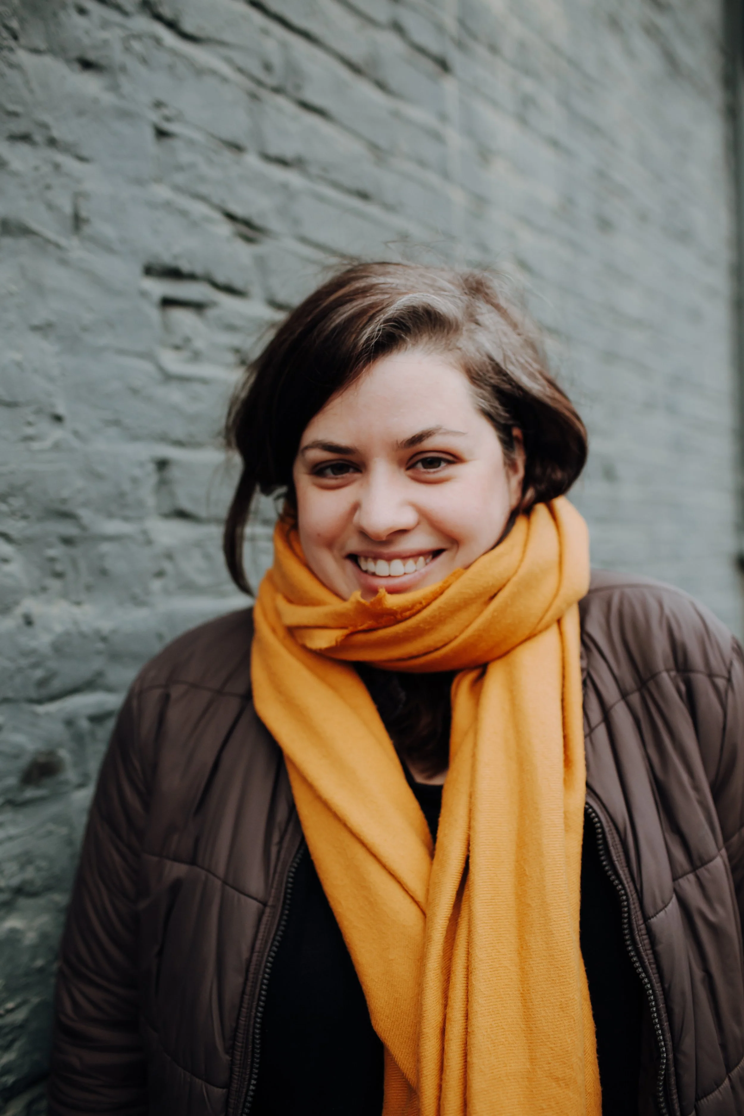 A portrait photograph of illustrator Joanna Bucur with a brown jacket and a yellow scarf around her neck