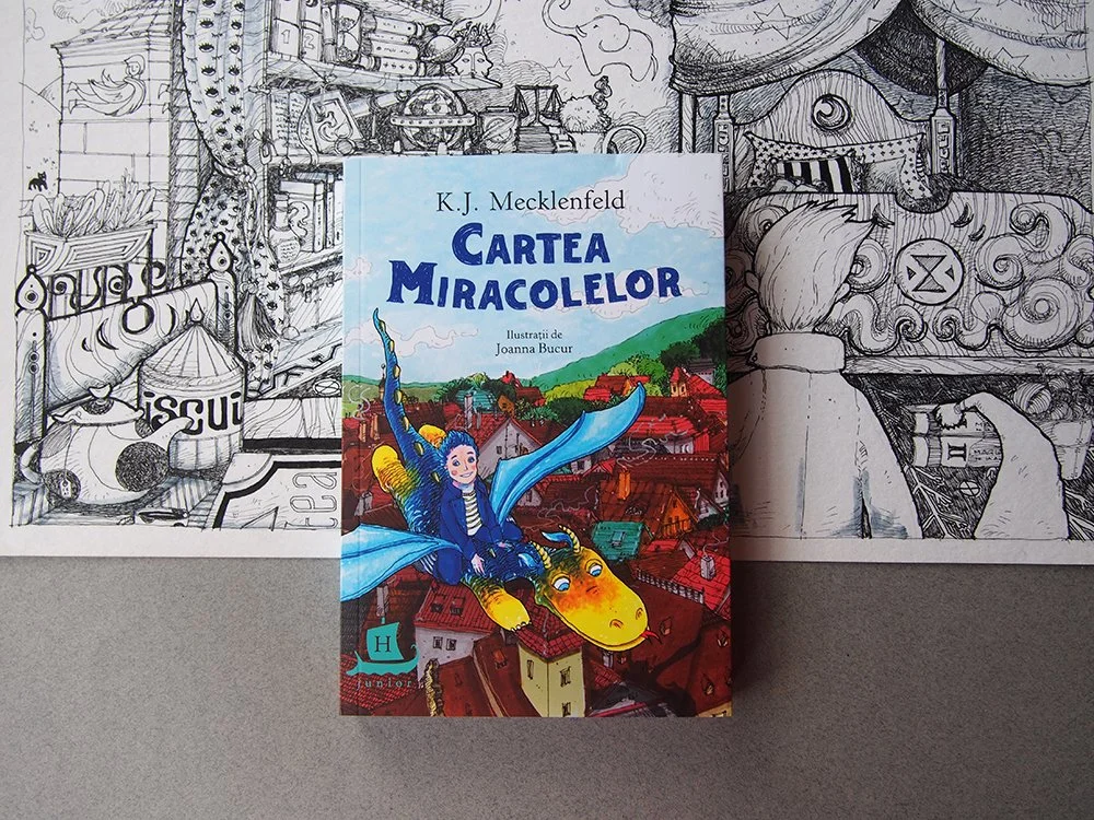 Colorful children's book titled 'Cartea Miracolelor' by K.J. Mecklenfeld, illustrated by Joanna Bucur, placed on a black and white line drawing of a detailed, whimsical interior scene and cityscape background.