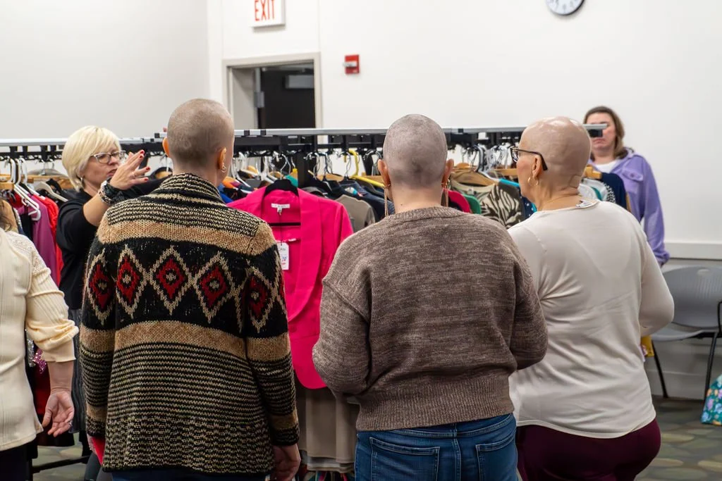 A group of women shopping for clothes in a store, with racks of clothing and a cashier counter in the background.