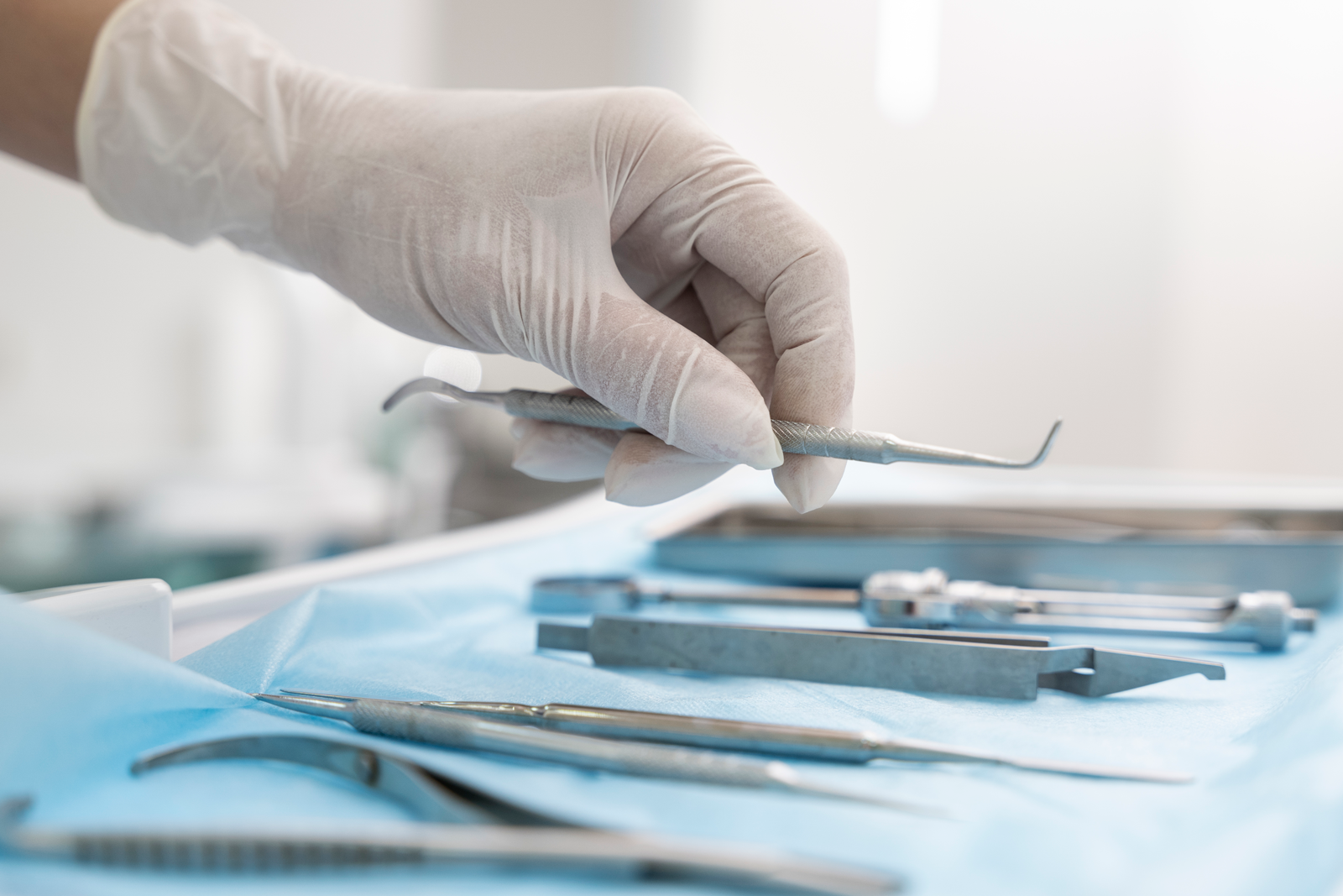 A gloved hand placing dental instruments on a tray