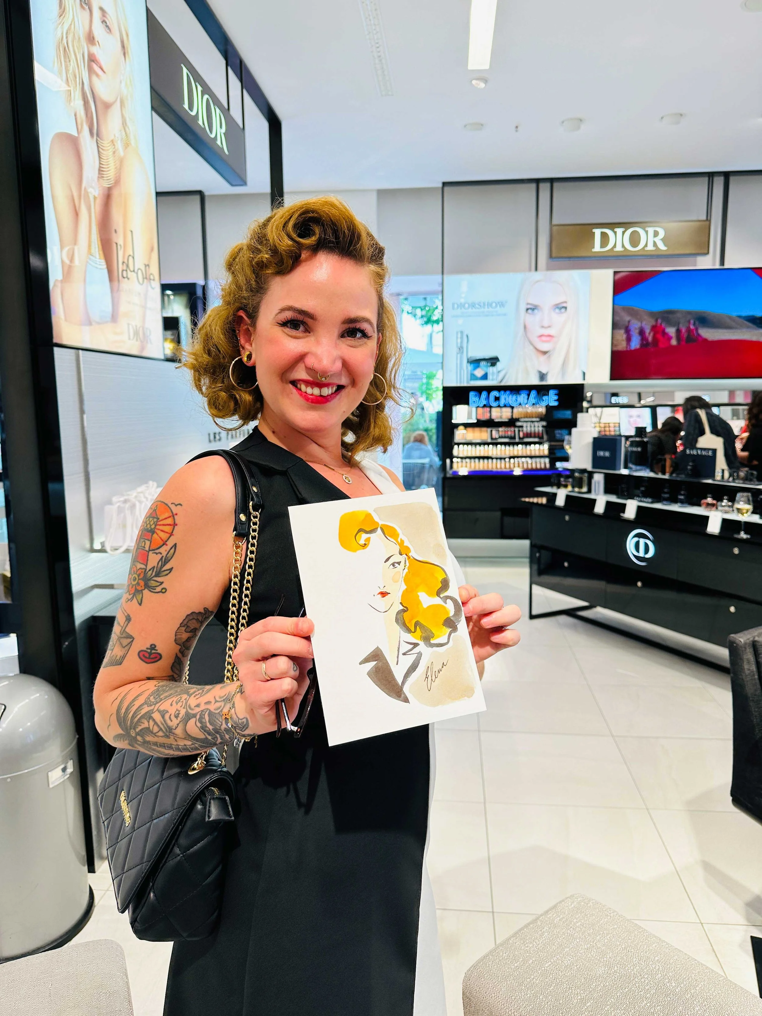 Smiling woman with tattoos holding an abstract illustration of a woman with yellow hair in a luxury store.