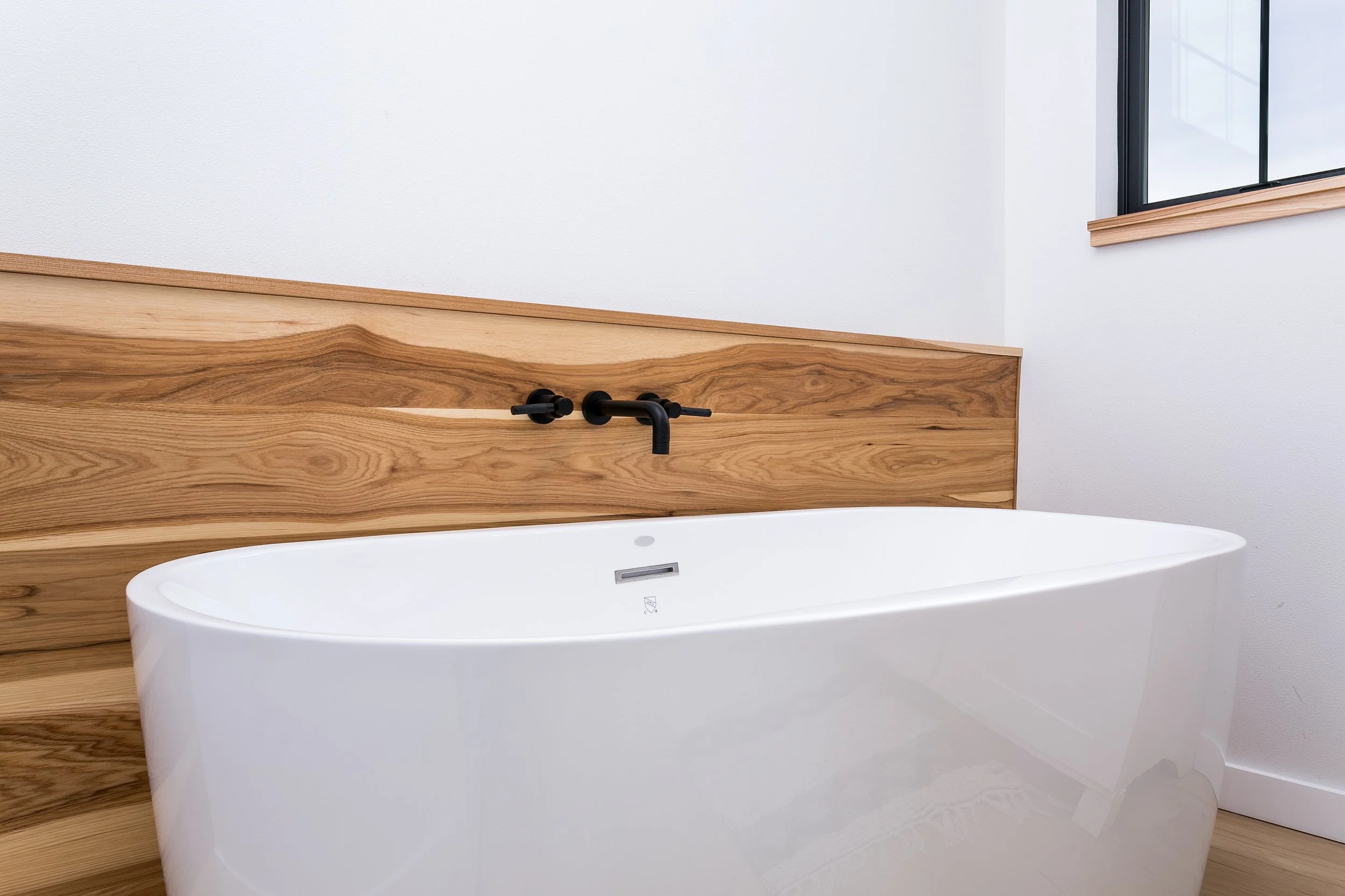 Modern bathroom with a freestanding white bathtub, mounted black faucet, and wooden accent wall.