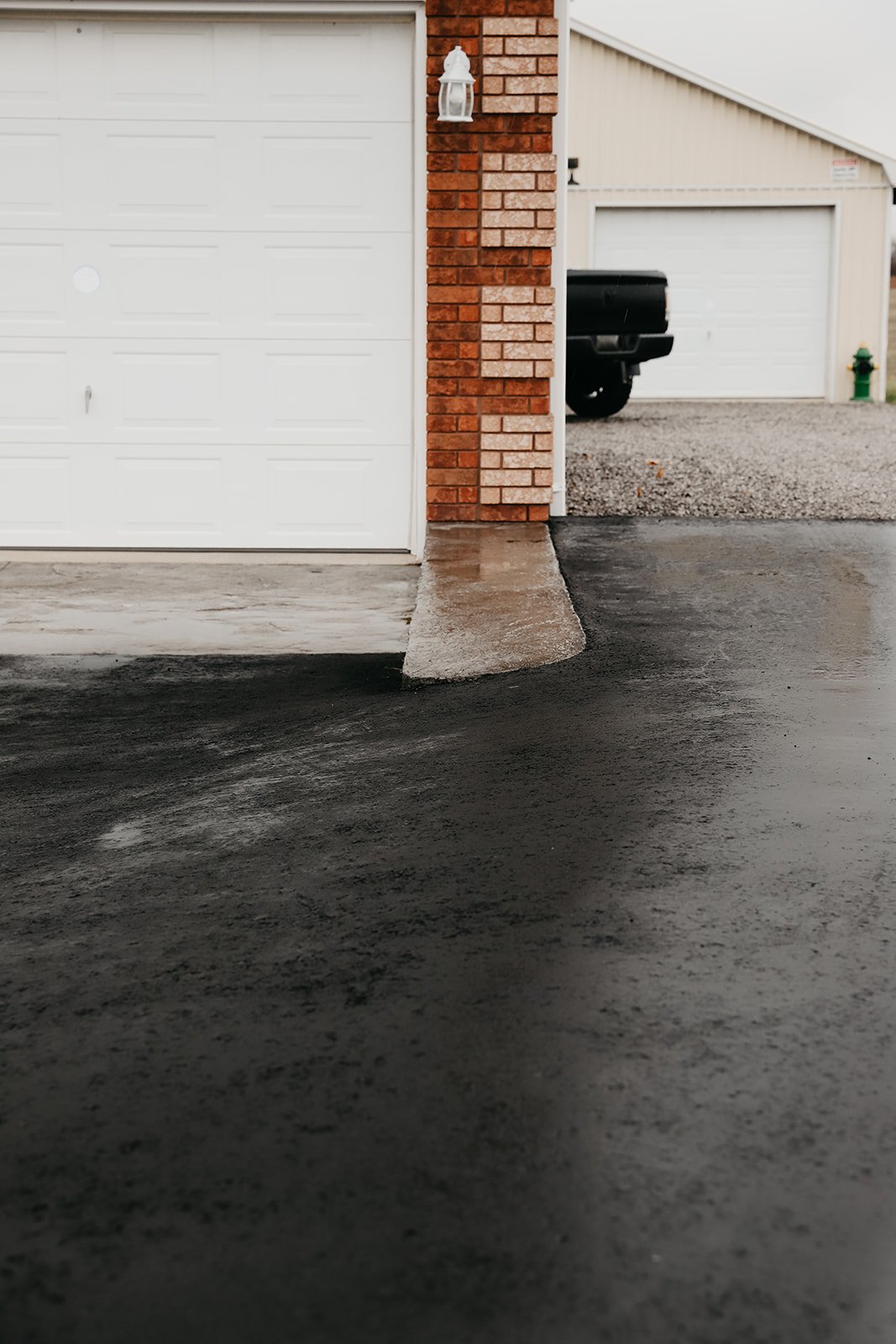 Garage and driveway entrance with wet asphalt, brick, and concrete surfaces.