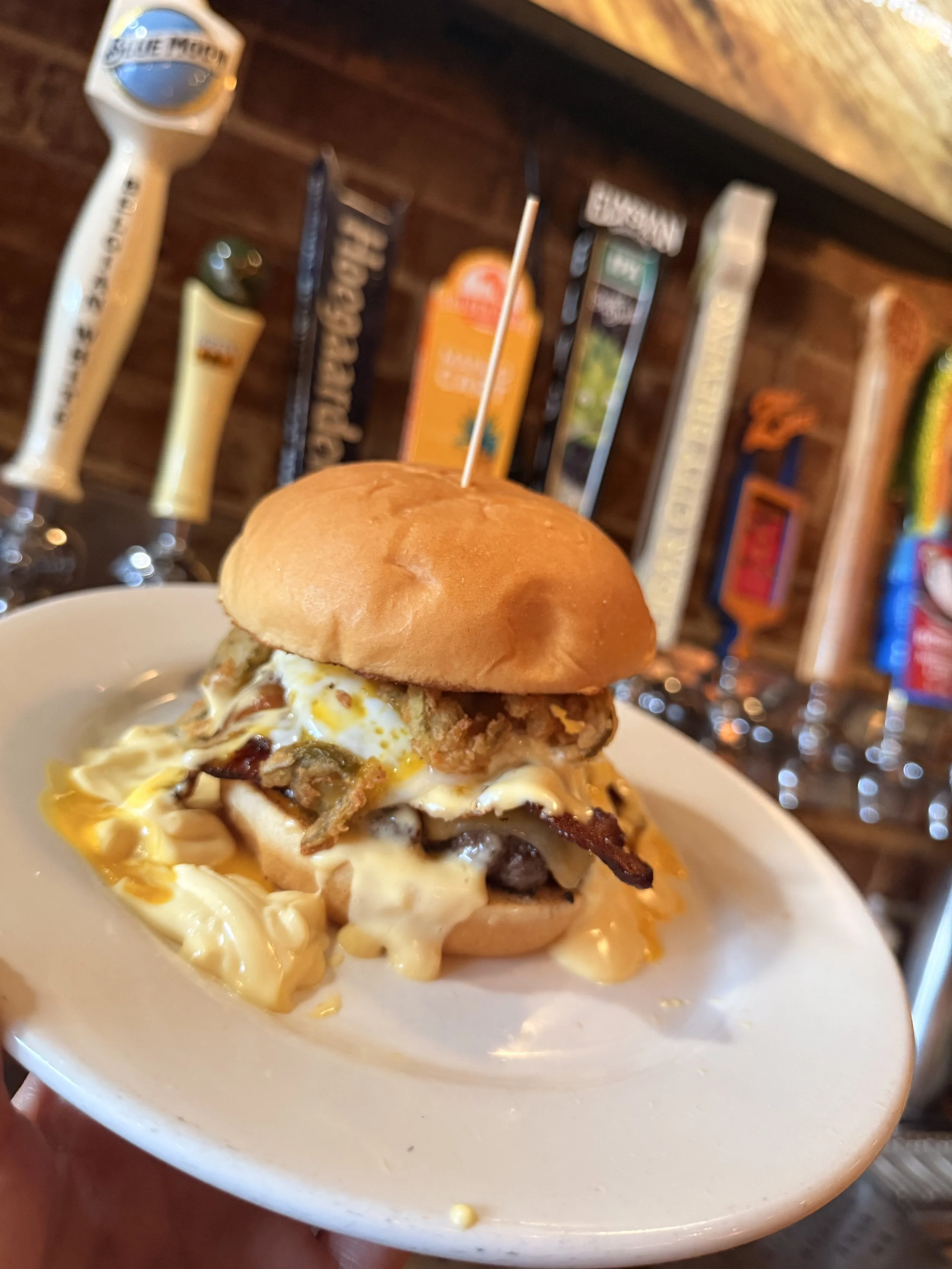 Feature Burger: Beef patty with gouda cheese, bacon, sunny side egg, and fried jalapenos topped with a drizzle of hollandaise on a Hawaiian bun. 