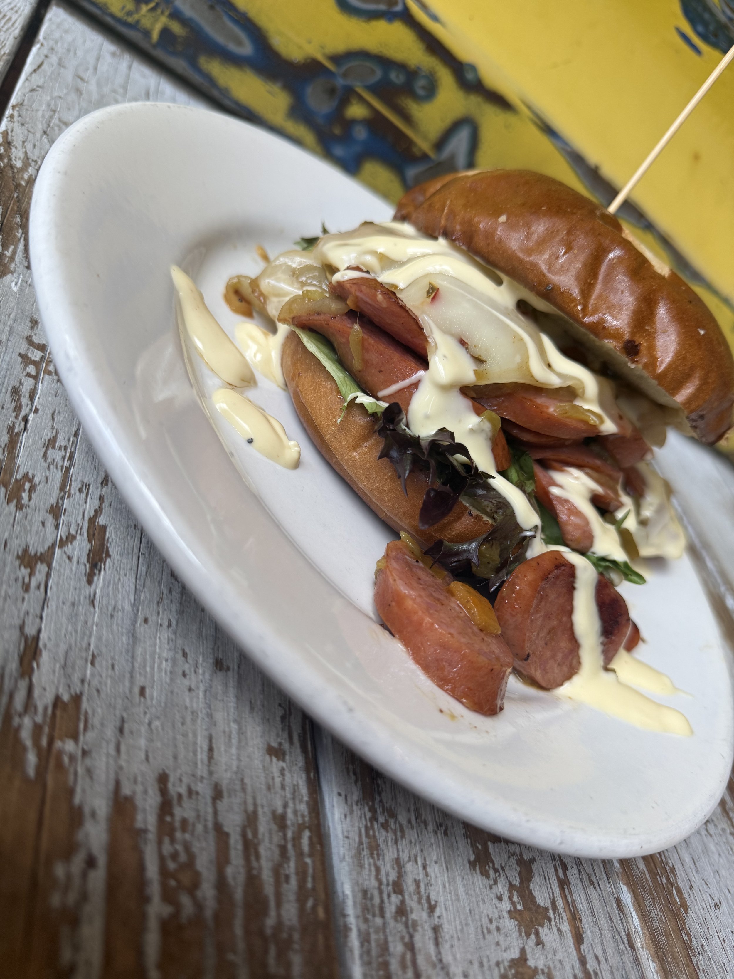 Feature Sammy: Sauteed andouille, pepper jack cheese, sauteed onions & green chilis, hollandaise on a toasted pretzel bun