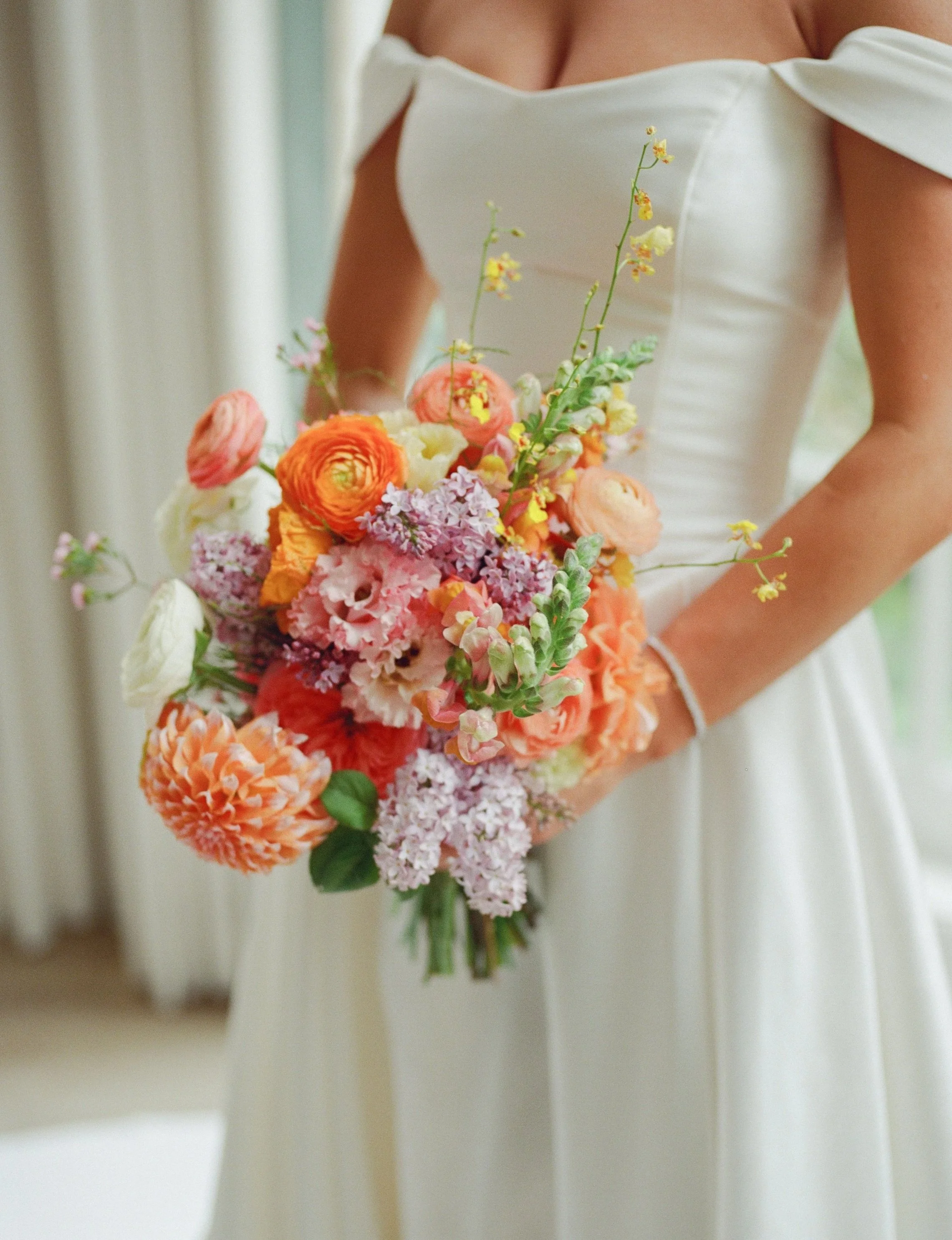 Close-up of a woman in a white off-shoulder dress holding a colorful bouquet of flowers.