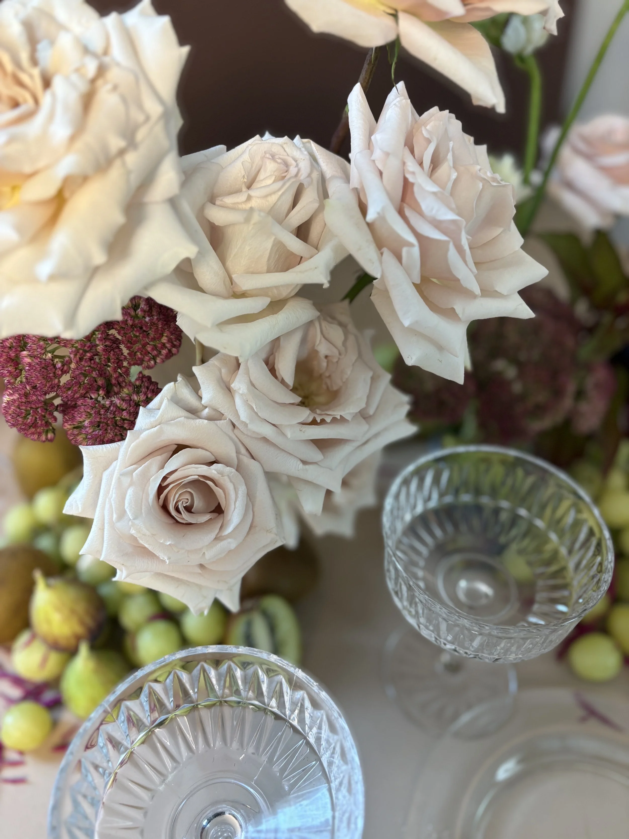 Close-up of a bouquet of white and pink roses, with some pink and green berries and two crystal glasses on a table.