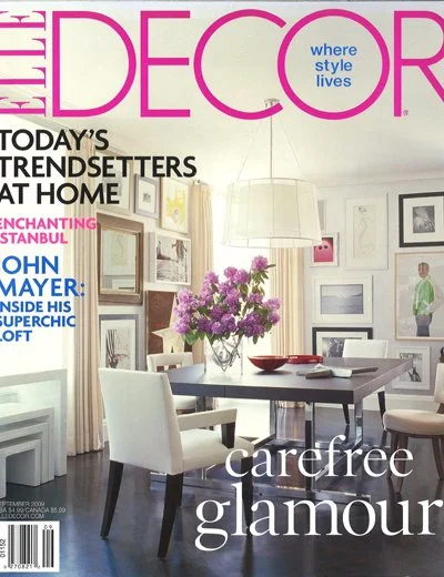 Cover of Elle Decor magazine featuring a modern dining room with a black table, white chairs, a large floral centerpiece, and gallery walls with framed art.