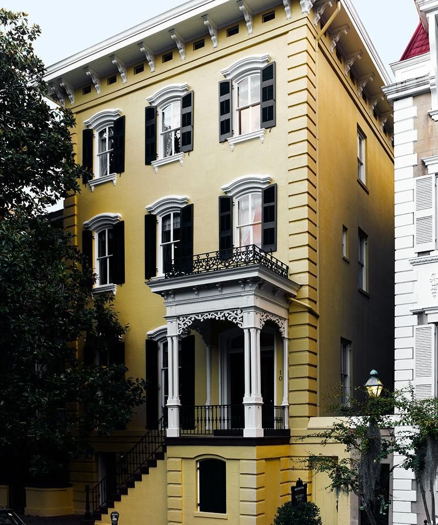 Yellow three-story house with ornate white trim, black shutters, and a small front porch.