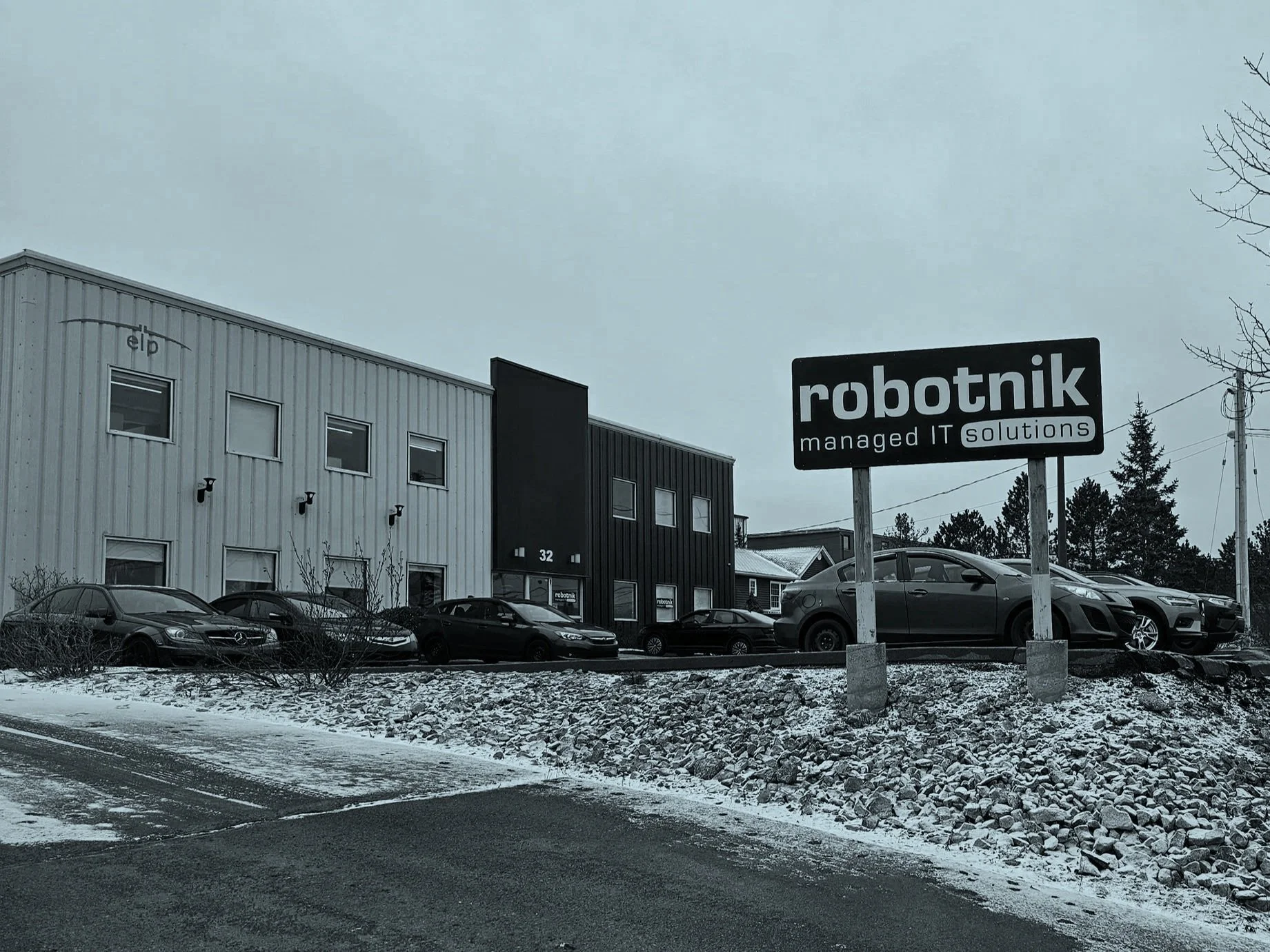 Exterior view of a building with a sign that says 'robotnik managed IT solutions,' parked cars, and a snowy ground.