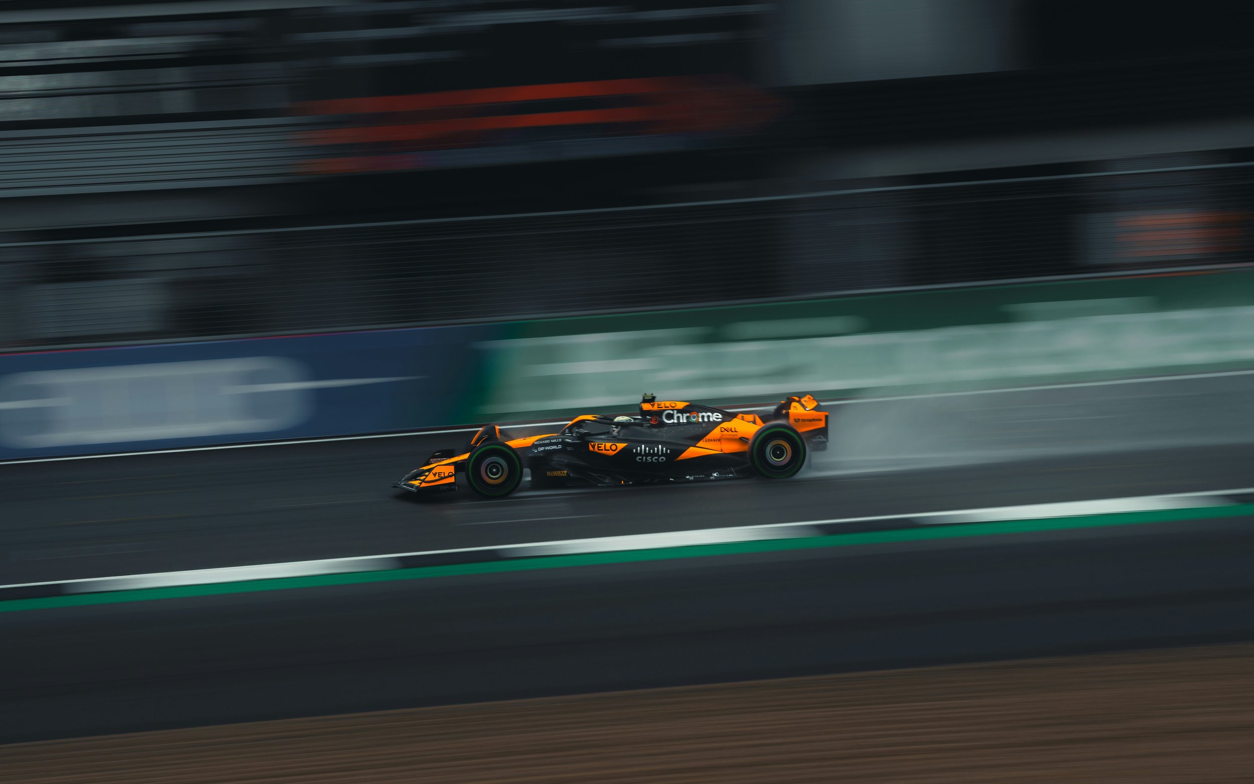 Orange and black Formula 1 race car speeding on a track with blurred background.