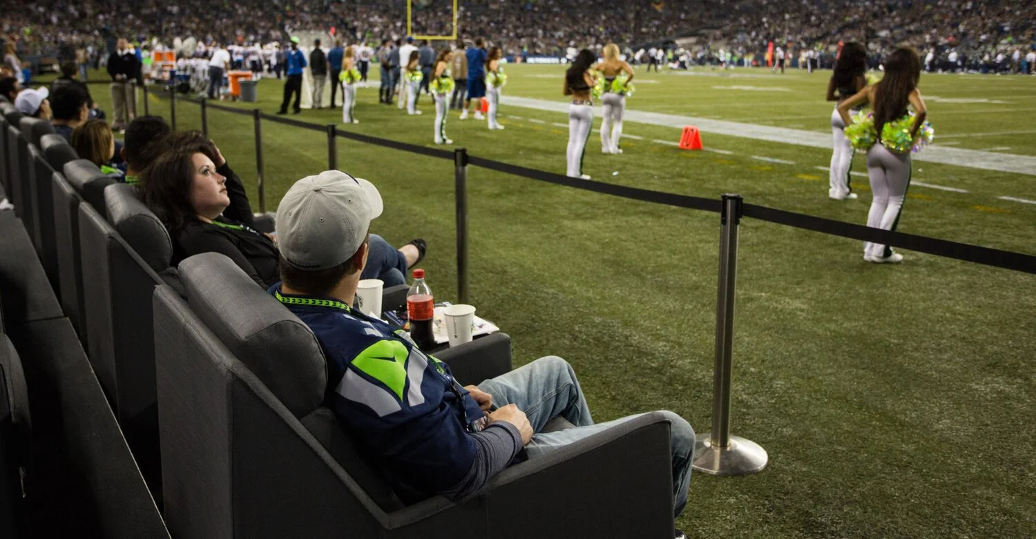 People seated on stadium seats watching cheerleaders on field