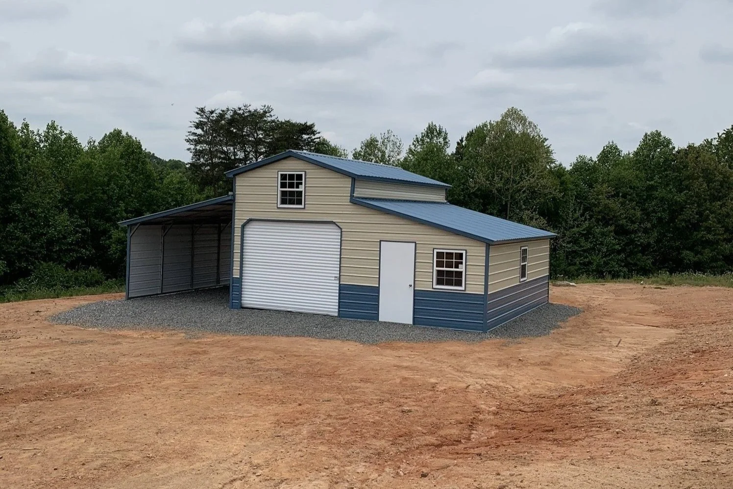 Metal barn with garage and carport surrounded by trees and bare ground.