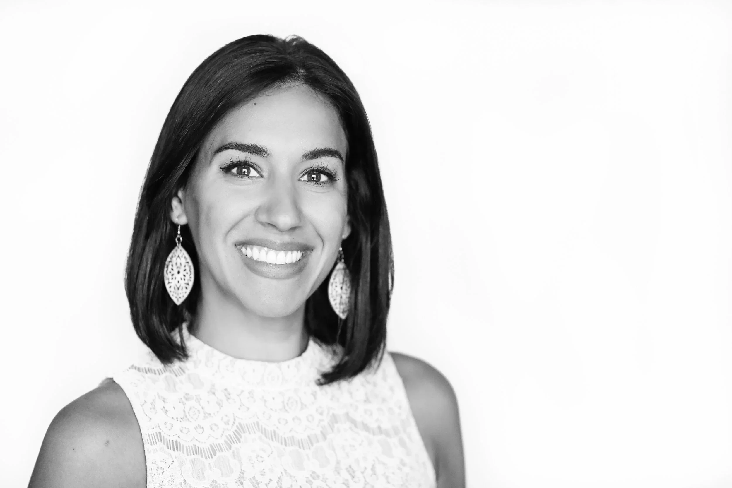 An energy healing client wearing black and white smiling, wearing a lace sleeveless top and large dangling earrings.