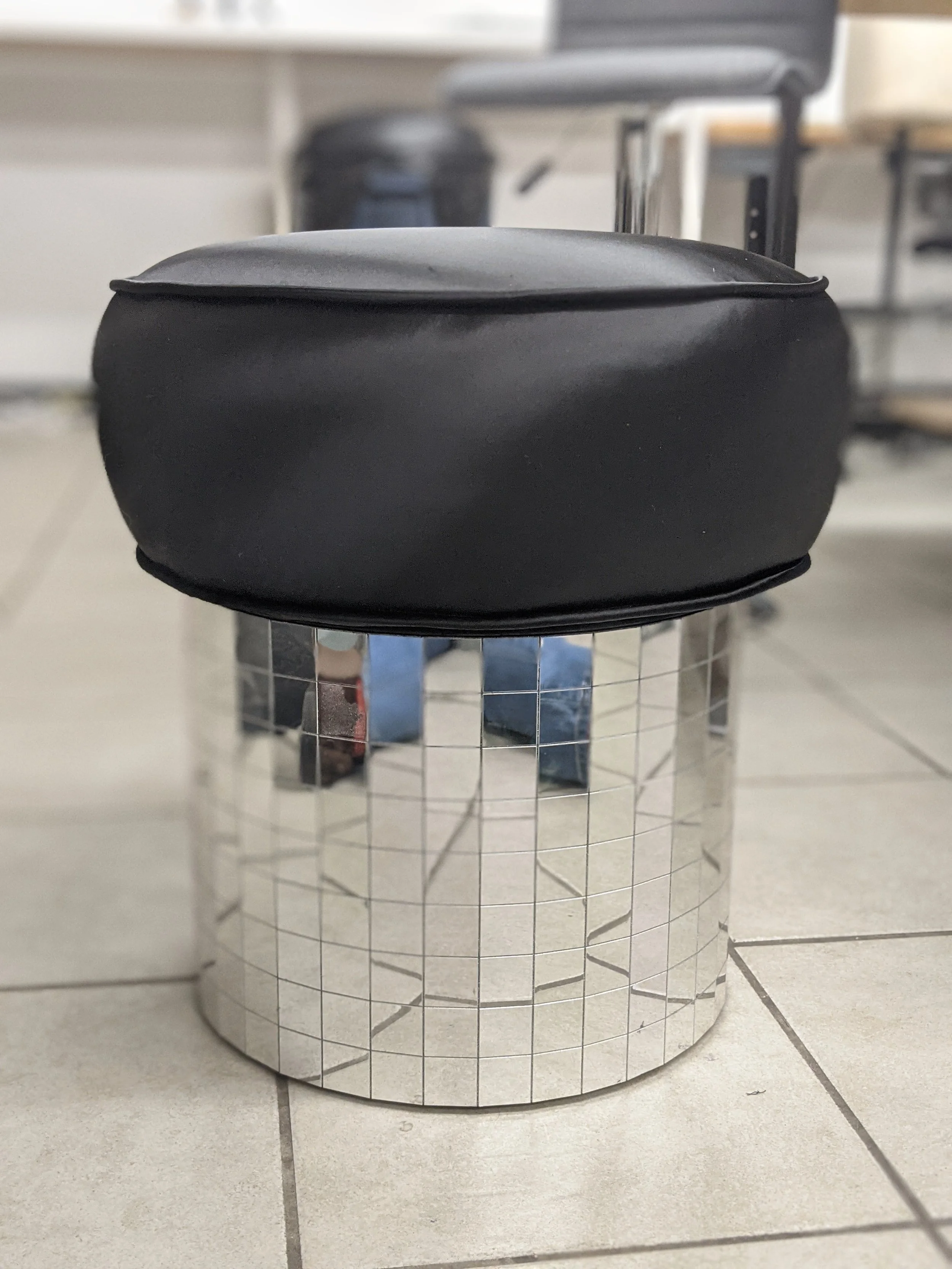 a short round stool with a black silk cushion on top and the base is covered in mirrored disco-ball tiles