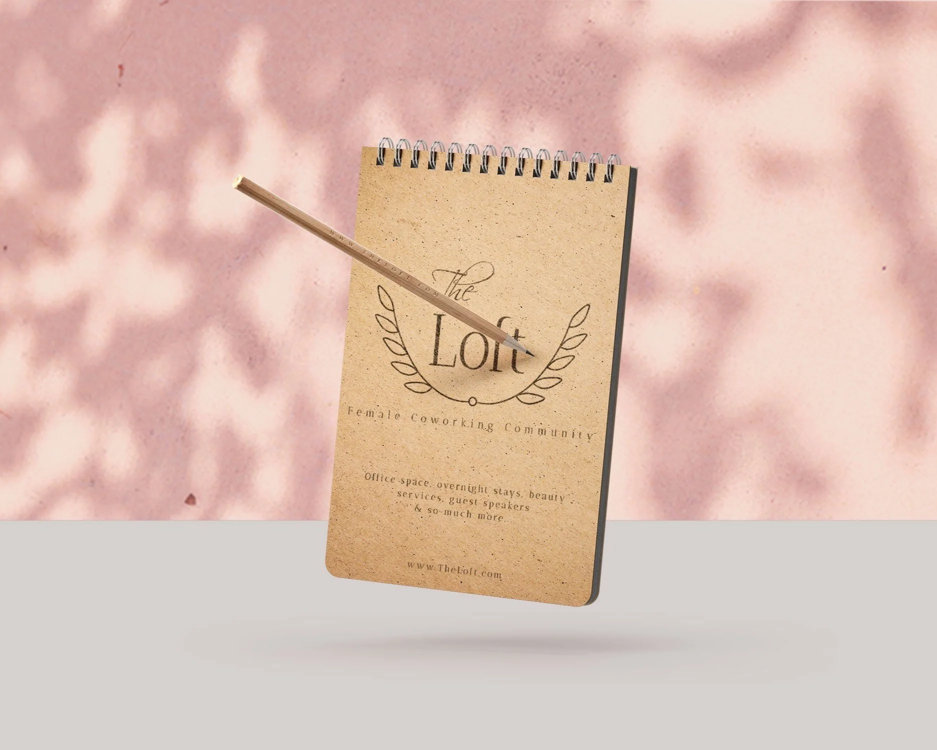 Brown notepad with "The Loft" logo and writing illegible in the image, on white counter and pink background with shadows