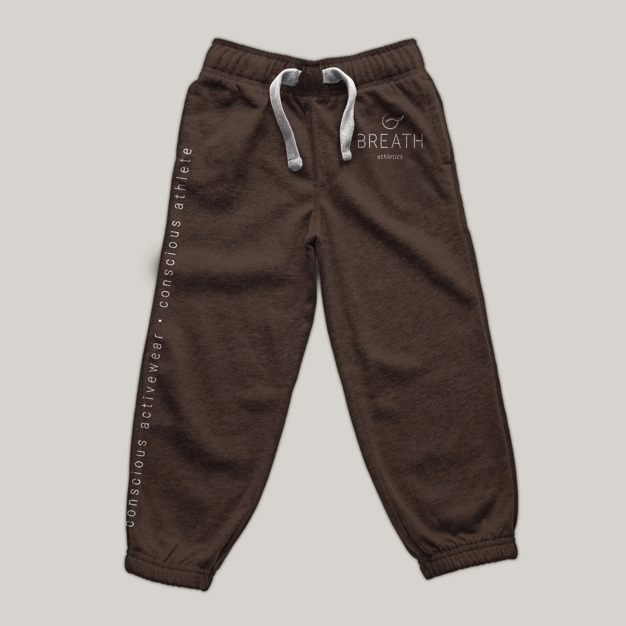 White logo mocked up on side of brown sweatpants with white drawstrings, and "conscious activewear • conscious athlete" in white vertical writing down the leg on the left