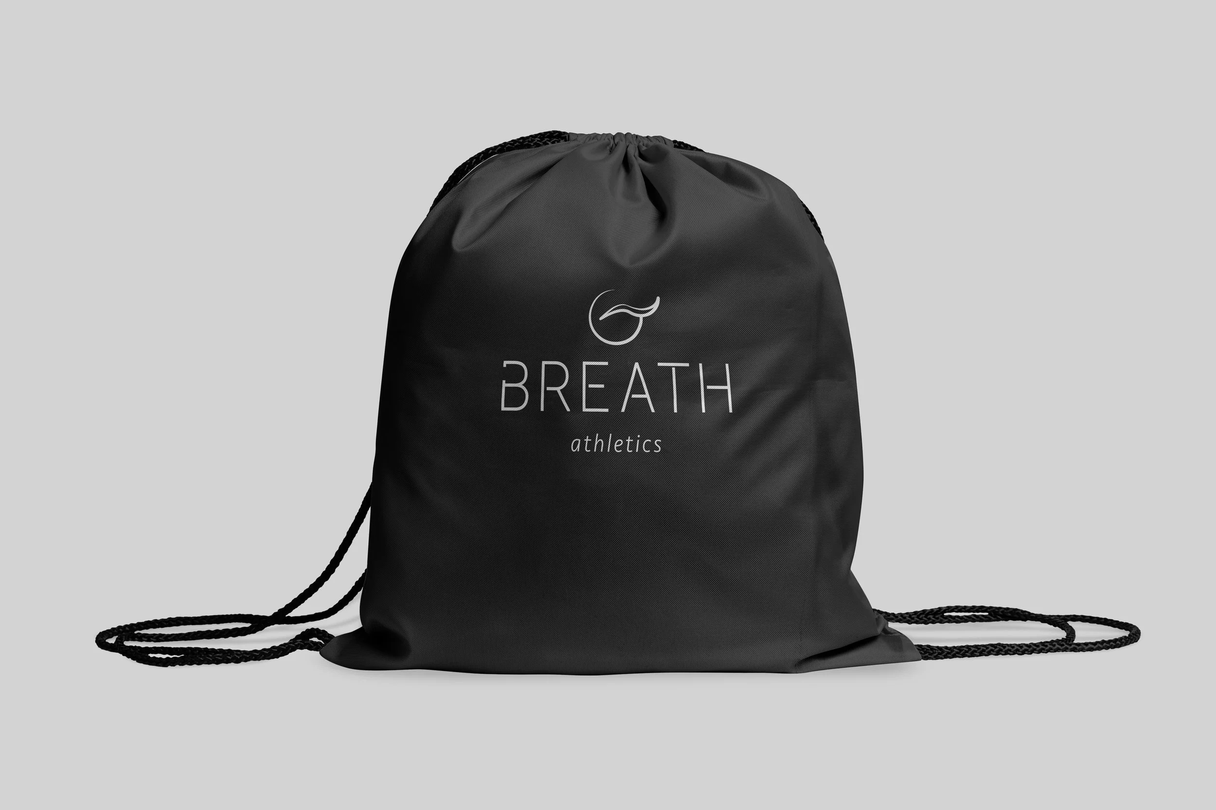 Black drawstring bag with white logo centered on front sits on the ground with a gray background