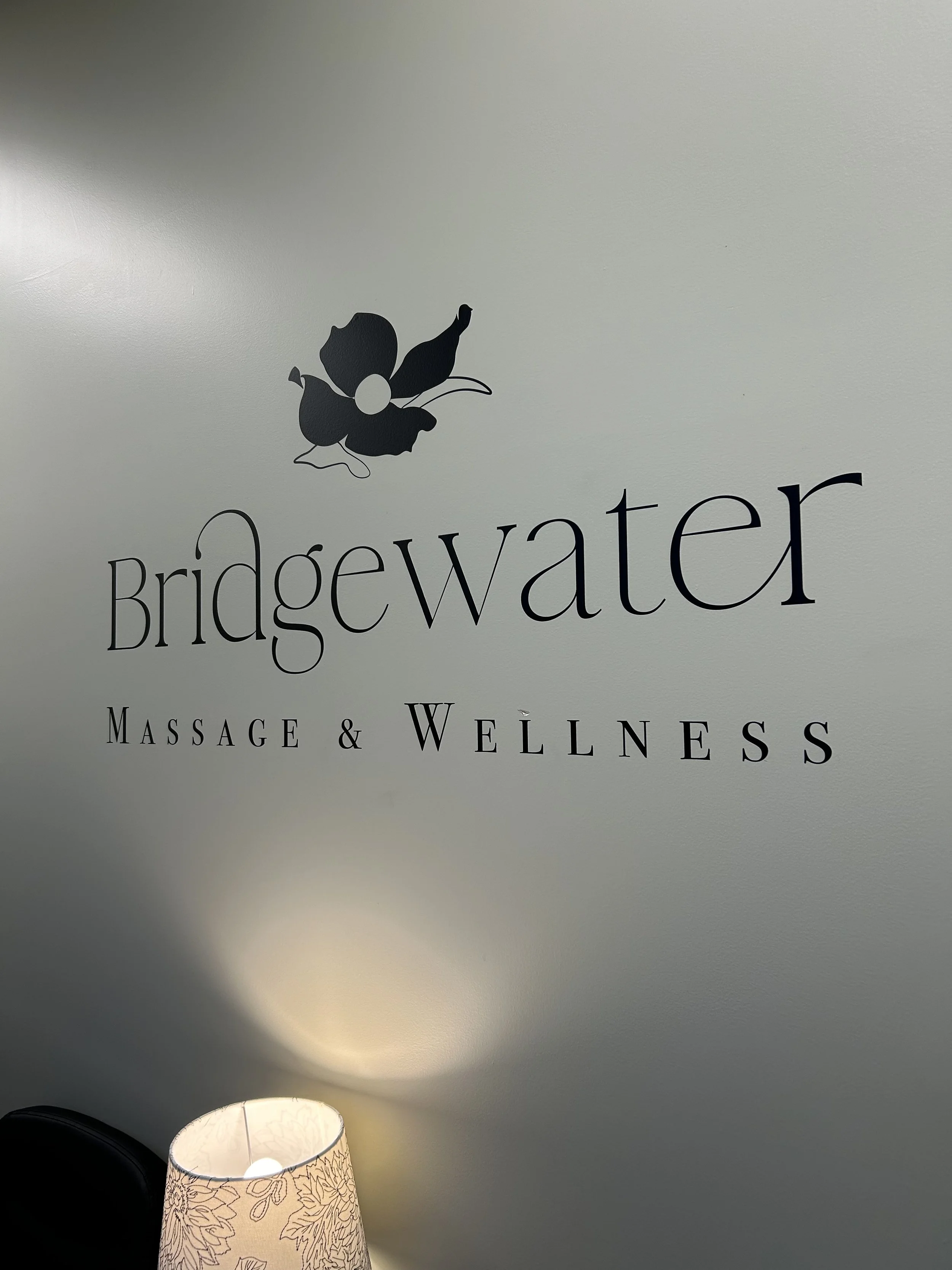 Vinyl sticker of all black logo photographed at an angle from the right. A white lamp shade is on the bottom left.