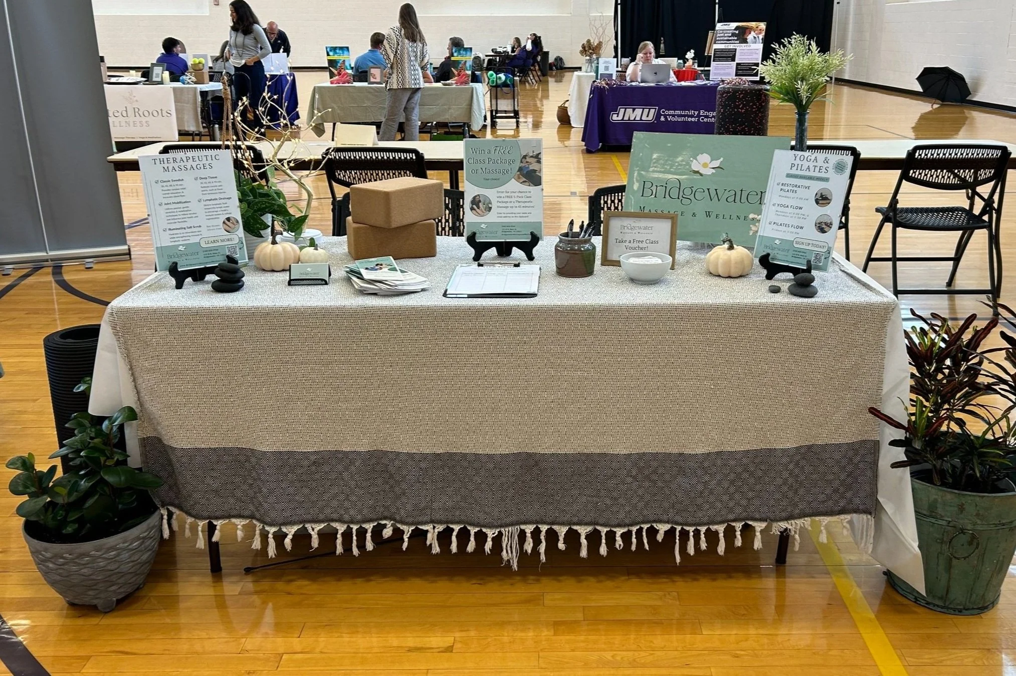 A gray clothed table features marketing materials designed by Heartleaf, including a giveaway sign, brochures, signup sheet, service menu, & class schedule. Also shows various table decor.