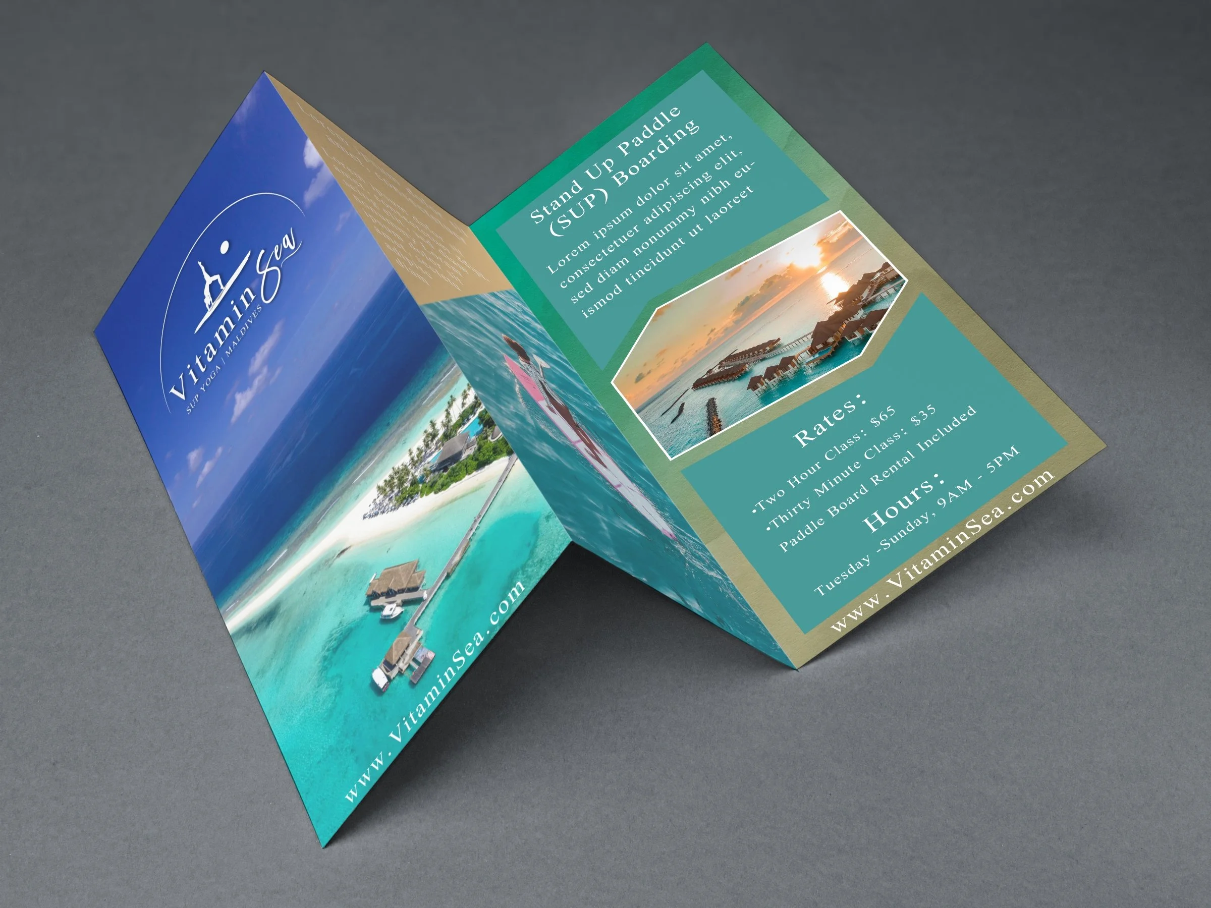 A trifold brochure lies unfolded on a gray background. The front page of the brochure shows an aerial image of the Maldives and the Vitamin Sea SUP logo is positioned at the top middle. The logo features a standup paddle boarder, arch, and name.