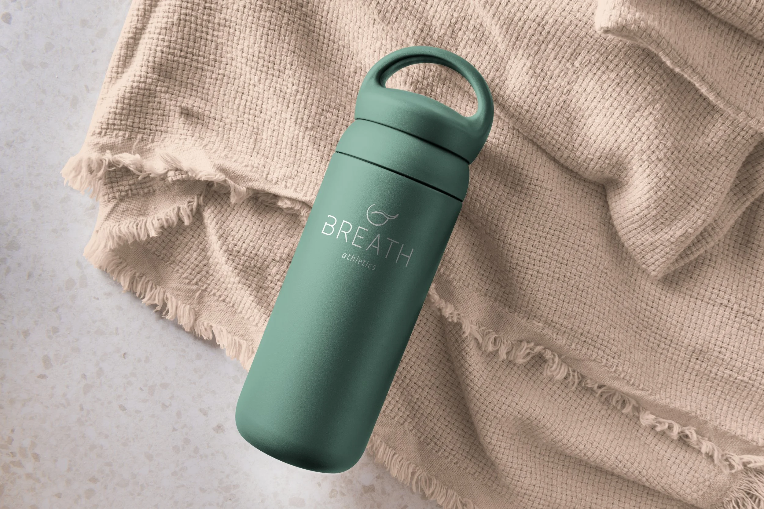 Green water bottle with white logo on center, lying on tan folded fabric
