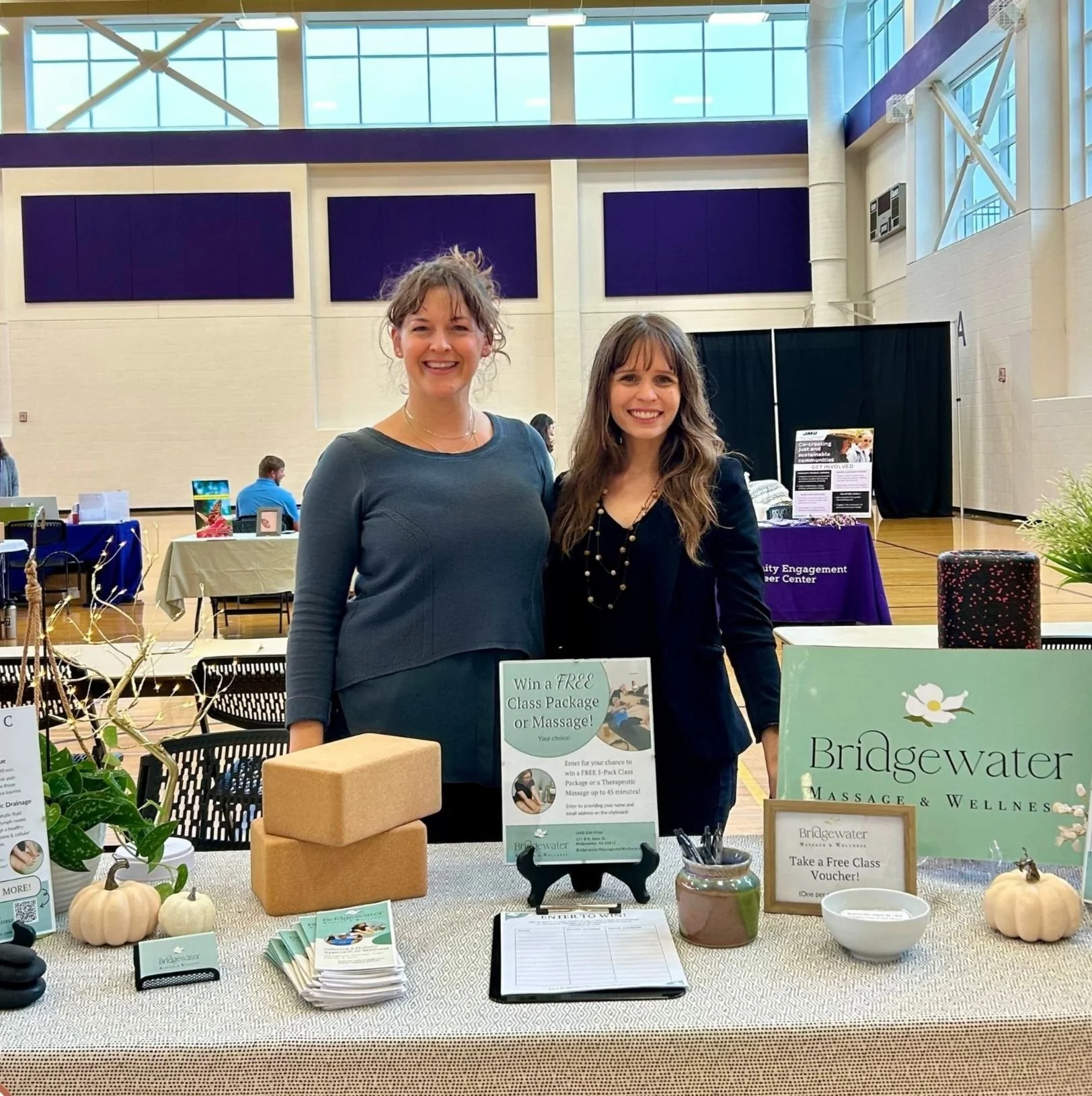 Business owner and Ashley stand together in a gymnasium behind a table displaying different marketing essentials designed by Heartleaf.