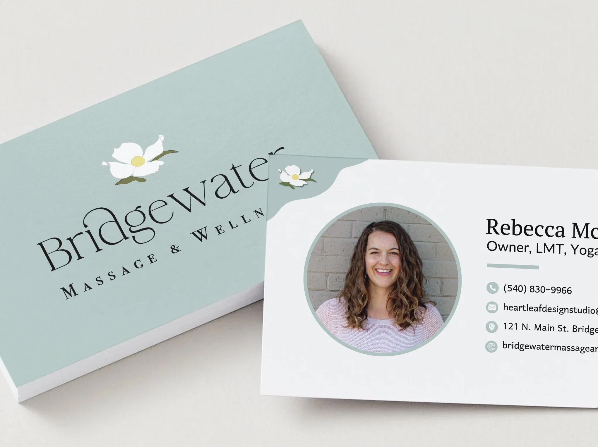 Left: front of Bridgewater Massage & Wellness business card design. Full color logo on light blue background. Right: back of business card depicting owner image, dogwood flower in top left, and part of name/info.
