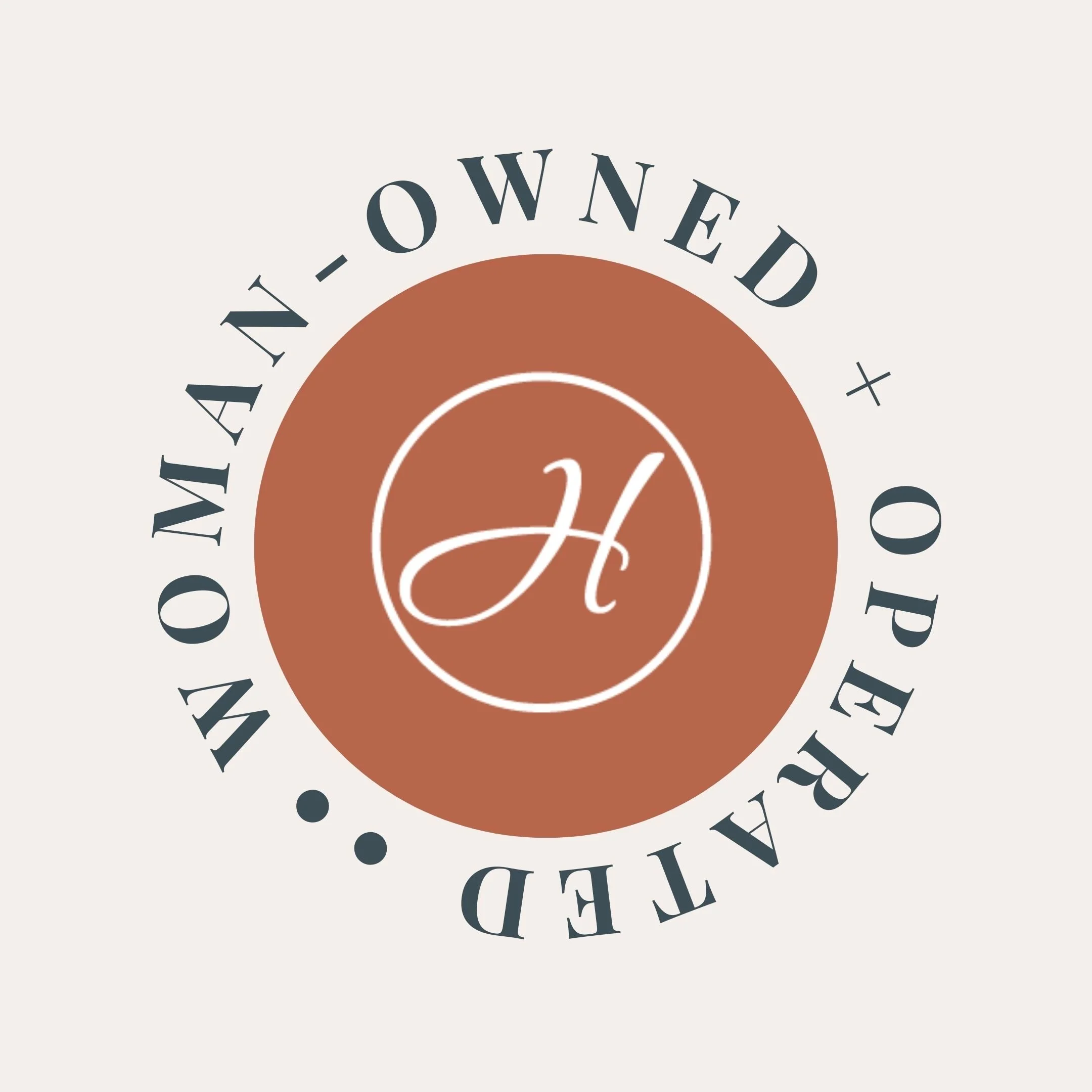A white scripted "H" is placed inside a white circular outline over an orange circle. "WOMAN-OWNED + OPERATED ••" letters surround the orange circle.