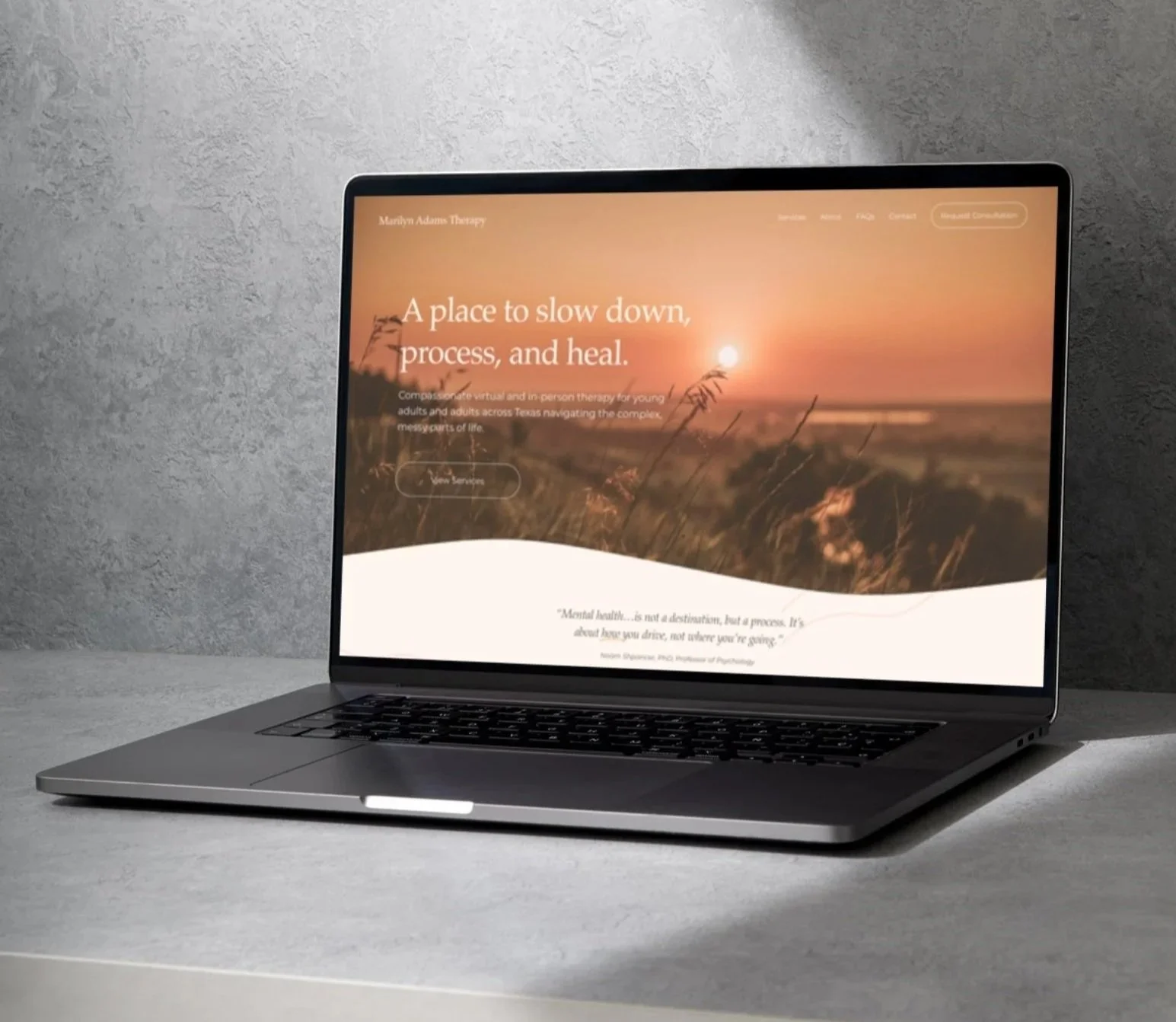 Laptop on a white table displaying a website with a sunset over a field background.