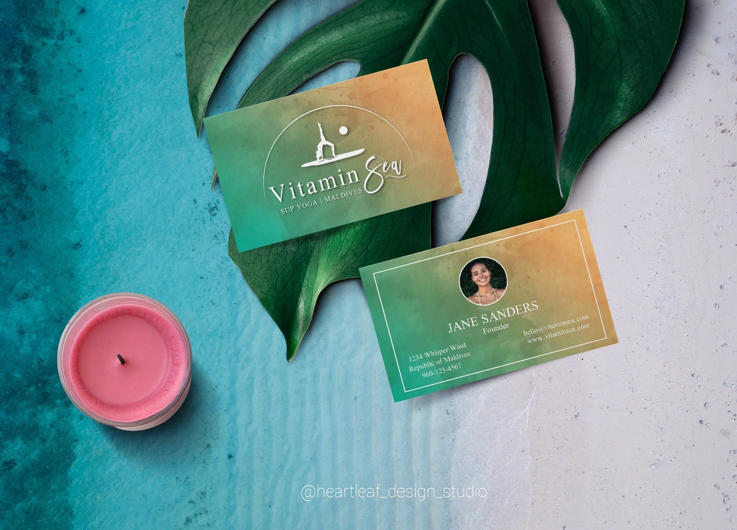 Business card front & back design. Front shows all white logo over blue and yellow watercolor background. Back shows same background with image of owner and info inside white rectangle. Placed over blue and white background with plant leaf and candle