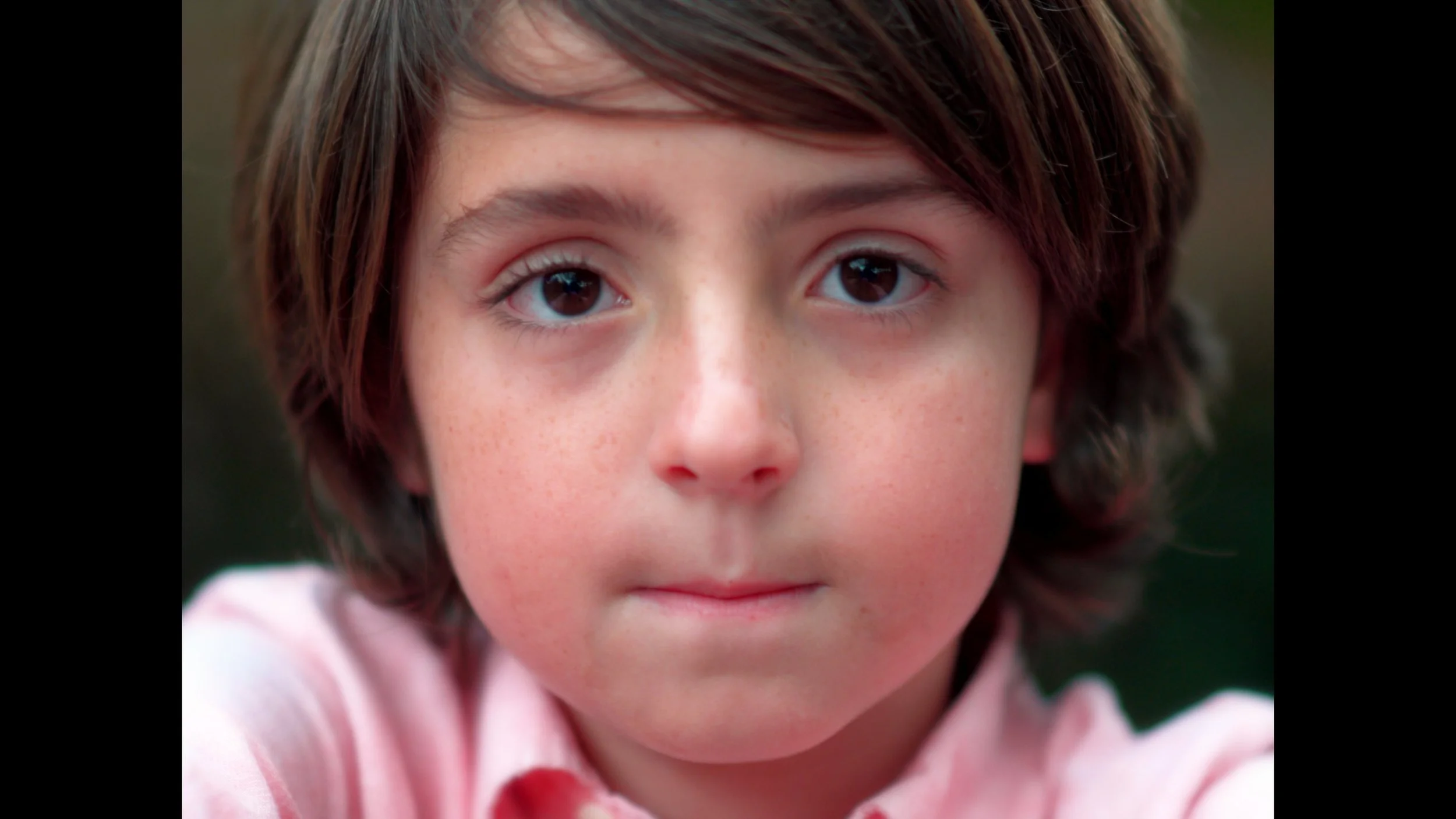 Cinematography, dirección de fotografía, DoP, cortometraje. Primer plano del rostro de un niño con cabello castaño, ojos oscuros, piel clara con pecas y expresión seria, usando una camisa rosa.