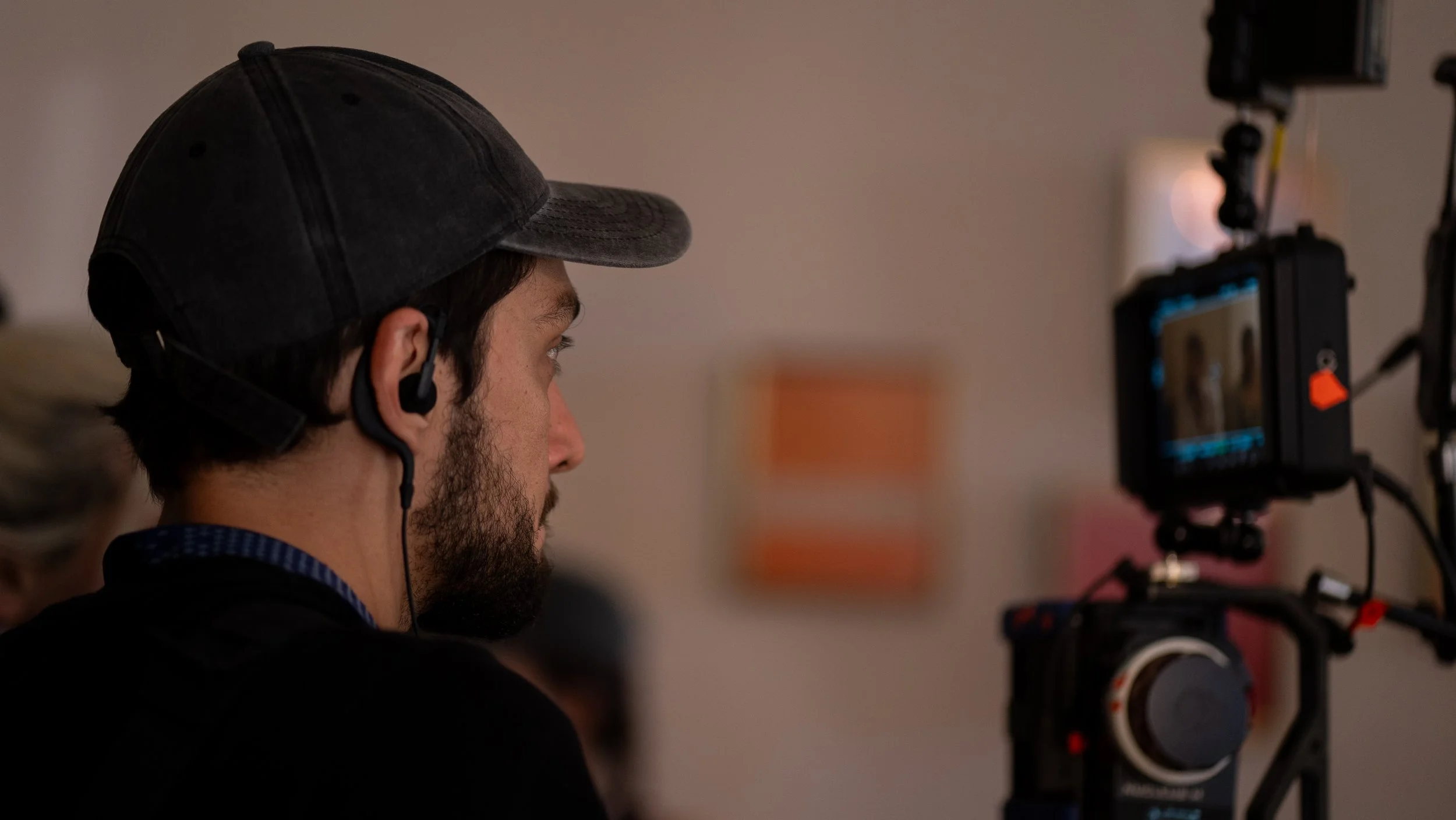 Persona con gorra y auriculares monitorea una cámara de grabación en un entorno de estudio.