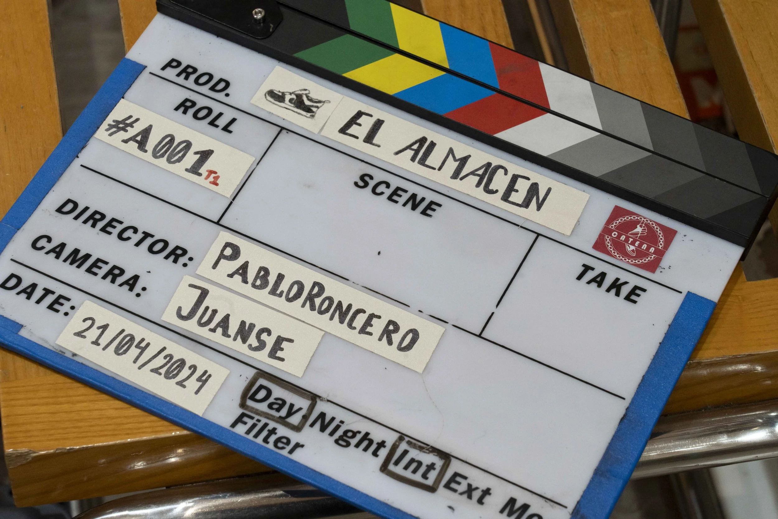 Pizarra de producción de filme con detalles del rodaje, incluyendo título "El Almacén", número de rodaje, director Juanse, guionista Pabloroncerro, fecha 21 de abril de 2024, y espacio para escena y toma.