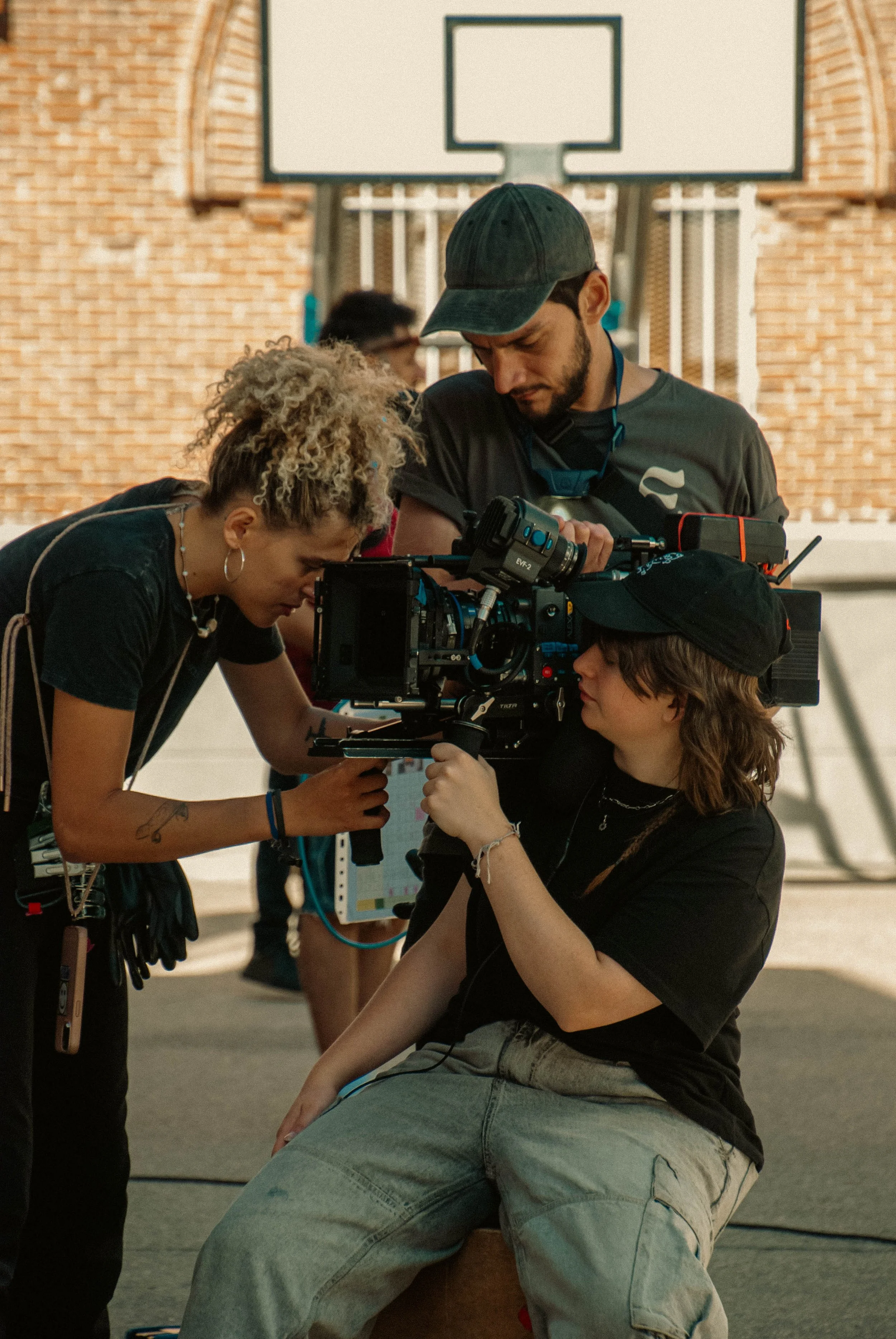 Equipo de filmación ajustando la cámara en un parque con cancha de baloncesto al fondo.